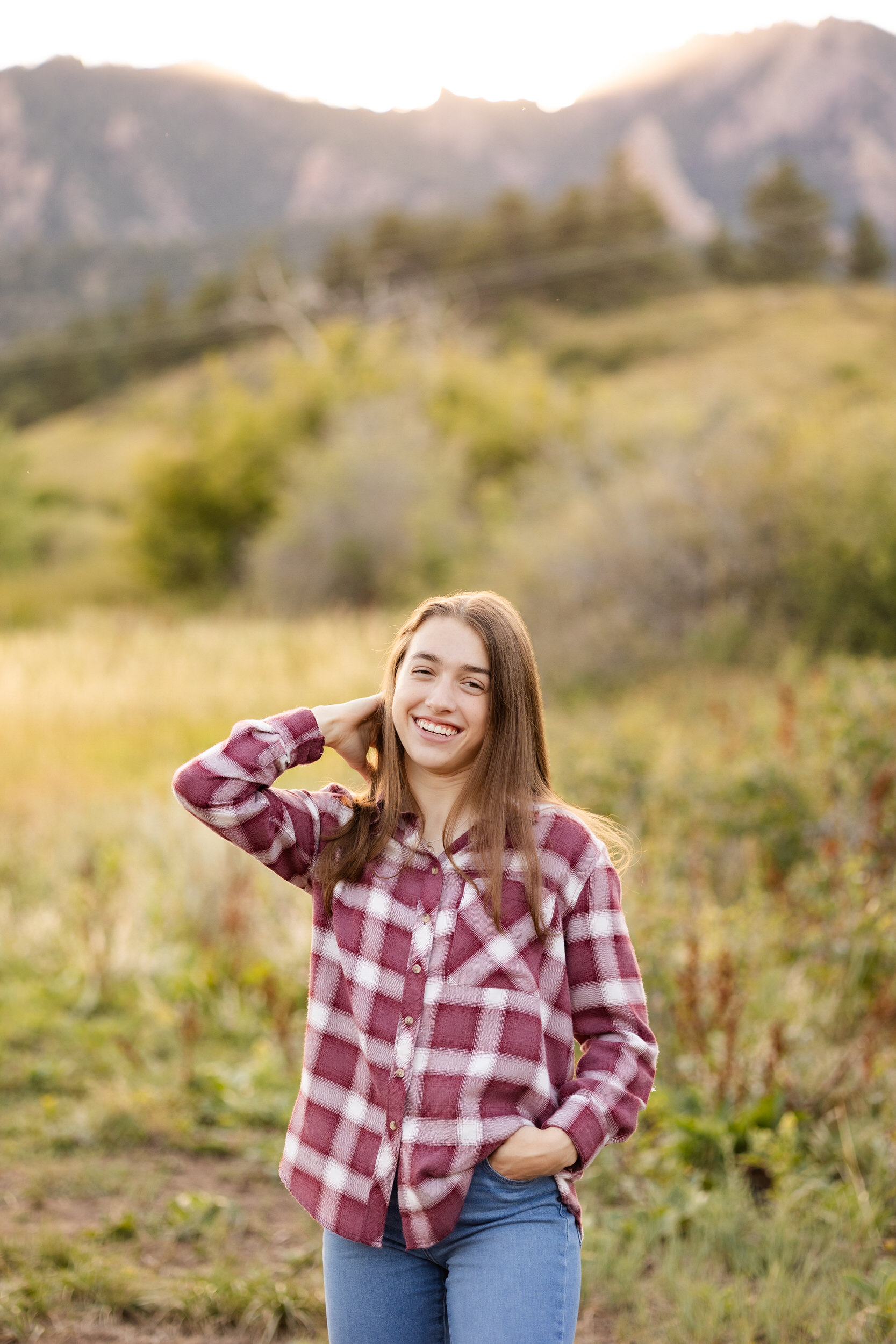 A young woman in a flannel shirt runs her hand through her hair and smiles at the camera.