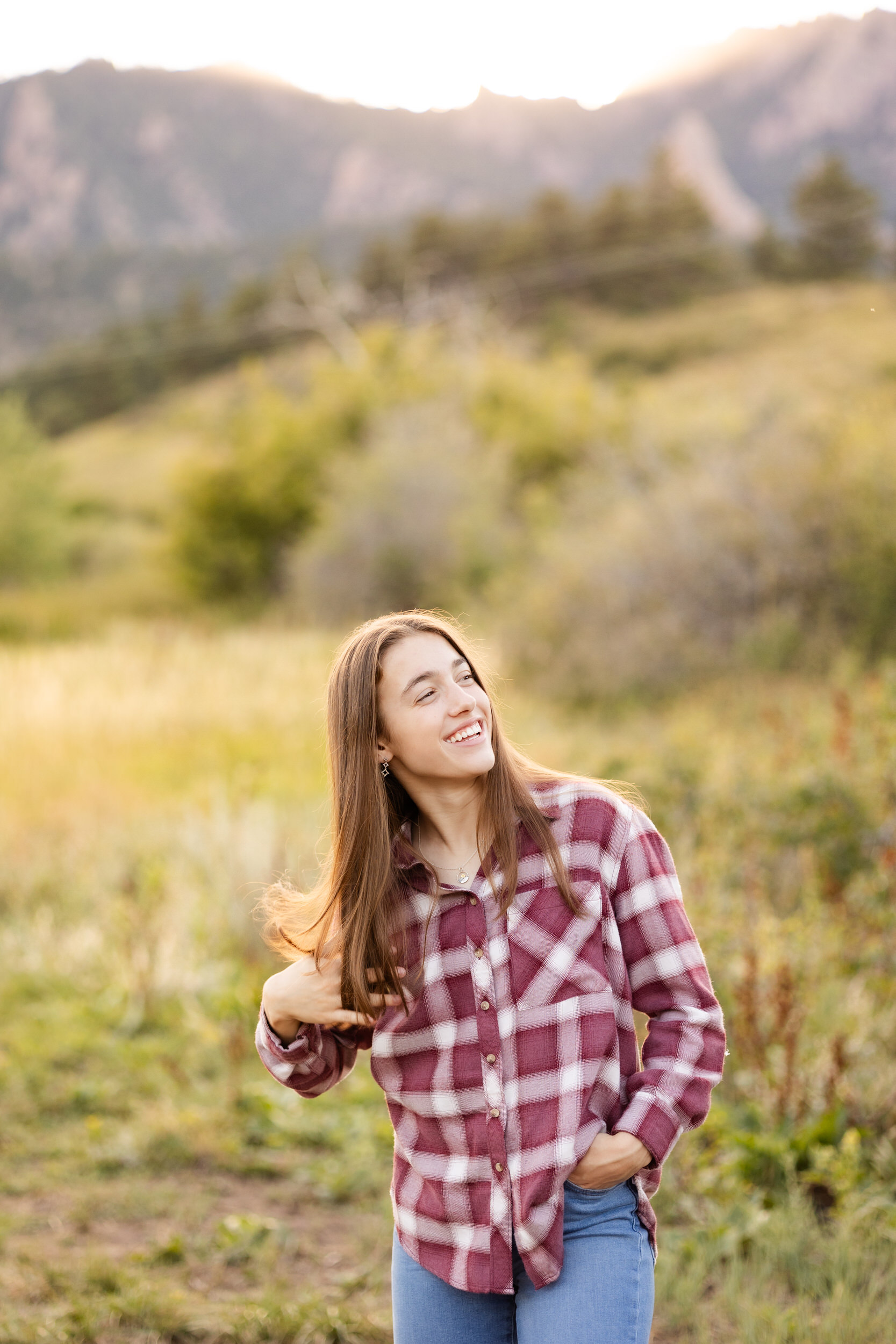 A young woman in a flannel shirt runs her hand through her hair and smiles off-camera.