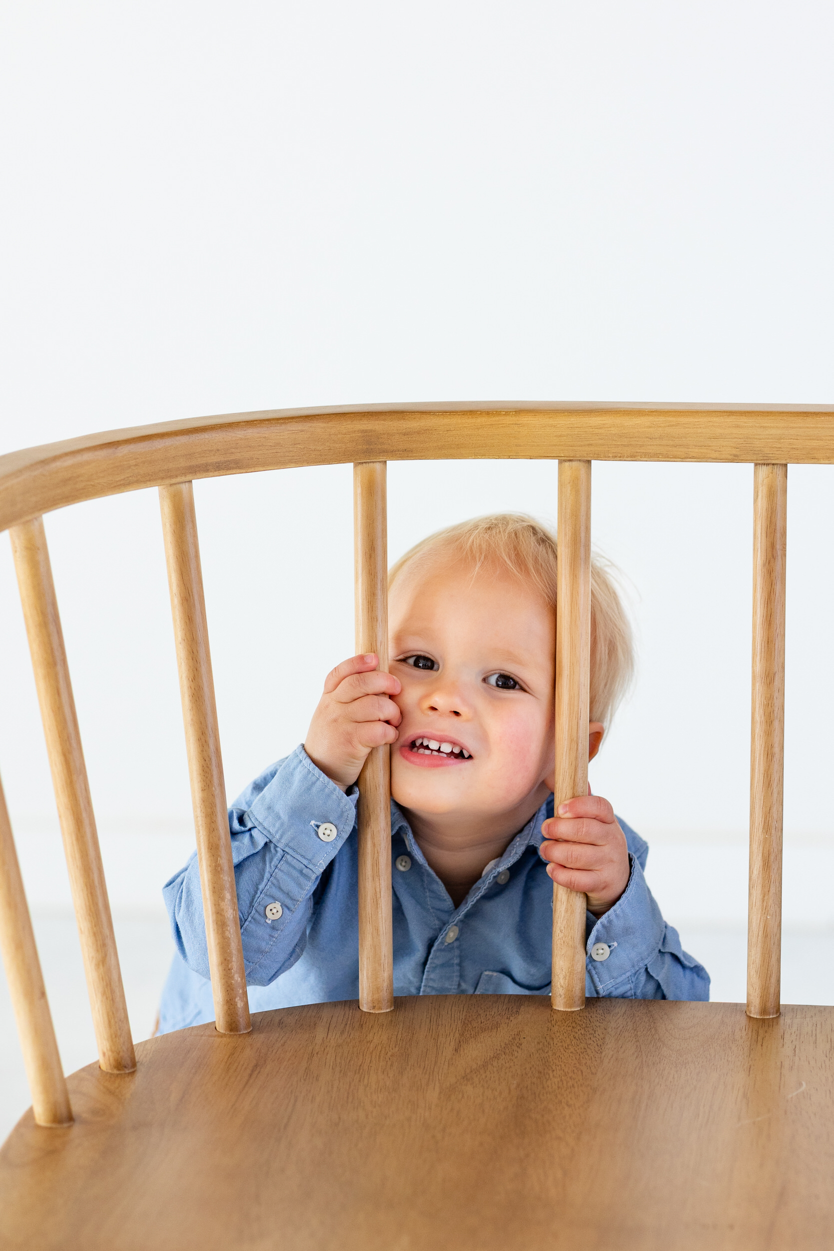 A little boy stands behind a bench and looks through the bars of the bench backrest.