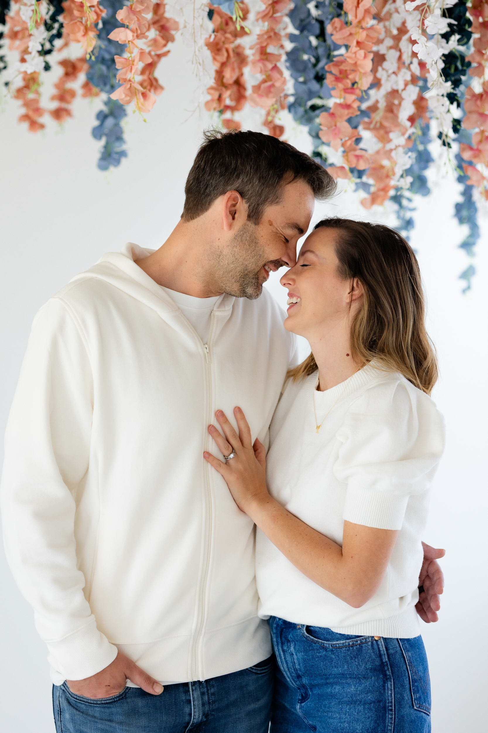 A husband and wife stand nose to nose and smile at each other.
