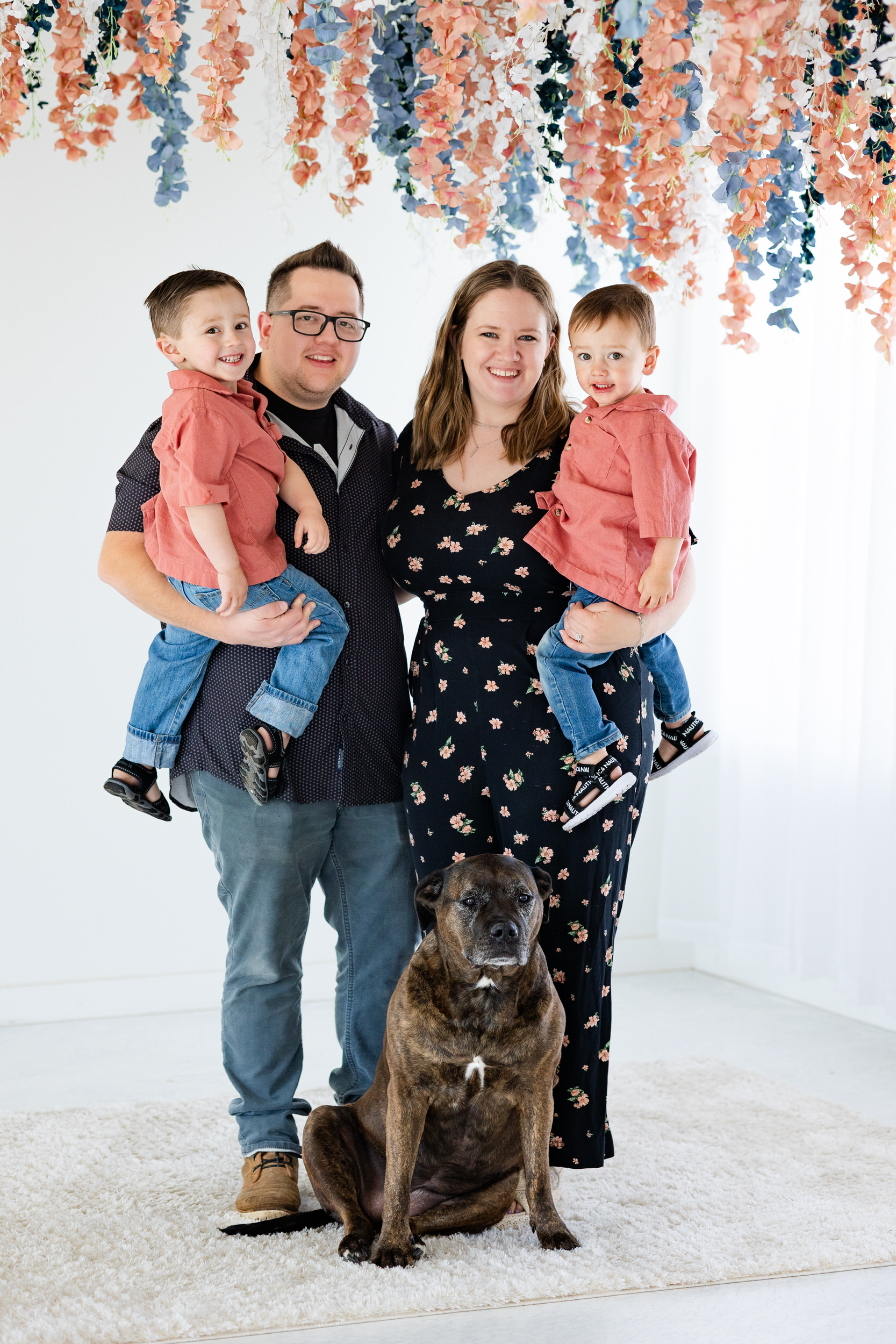 A family of four smiles at the camera with their dog sitting in front of them.