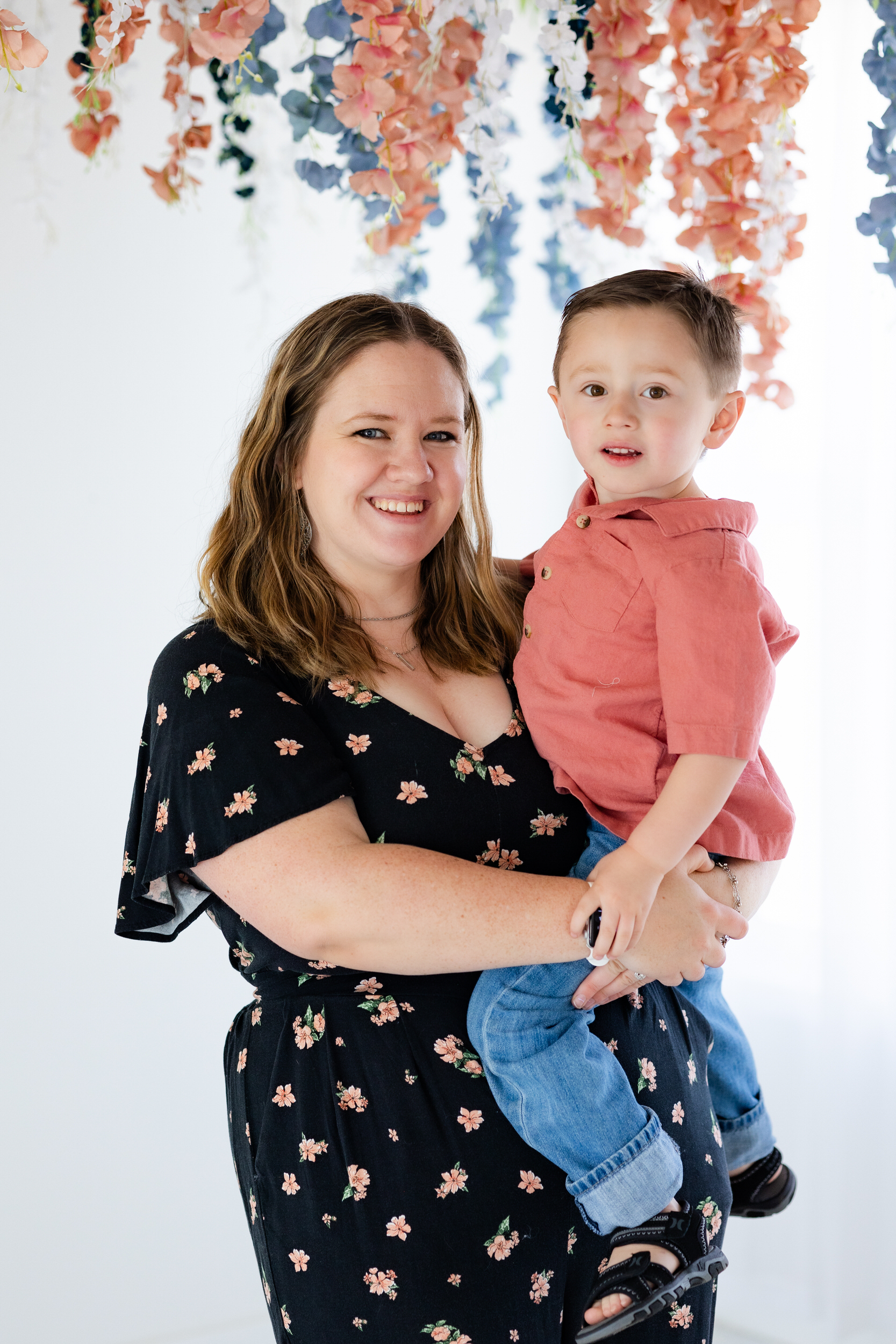 A mom holds her young son and they both smile at the camera.