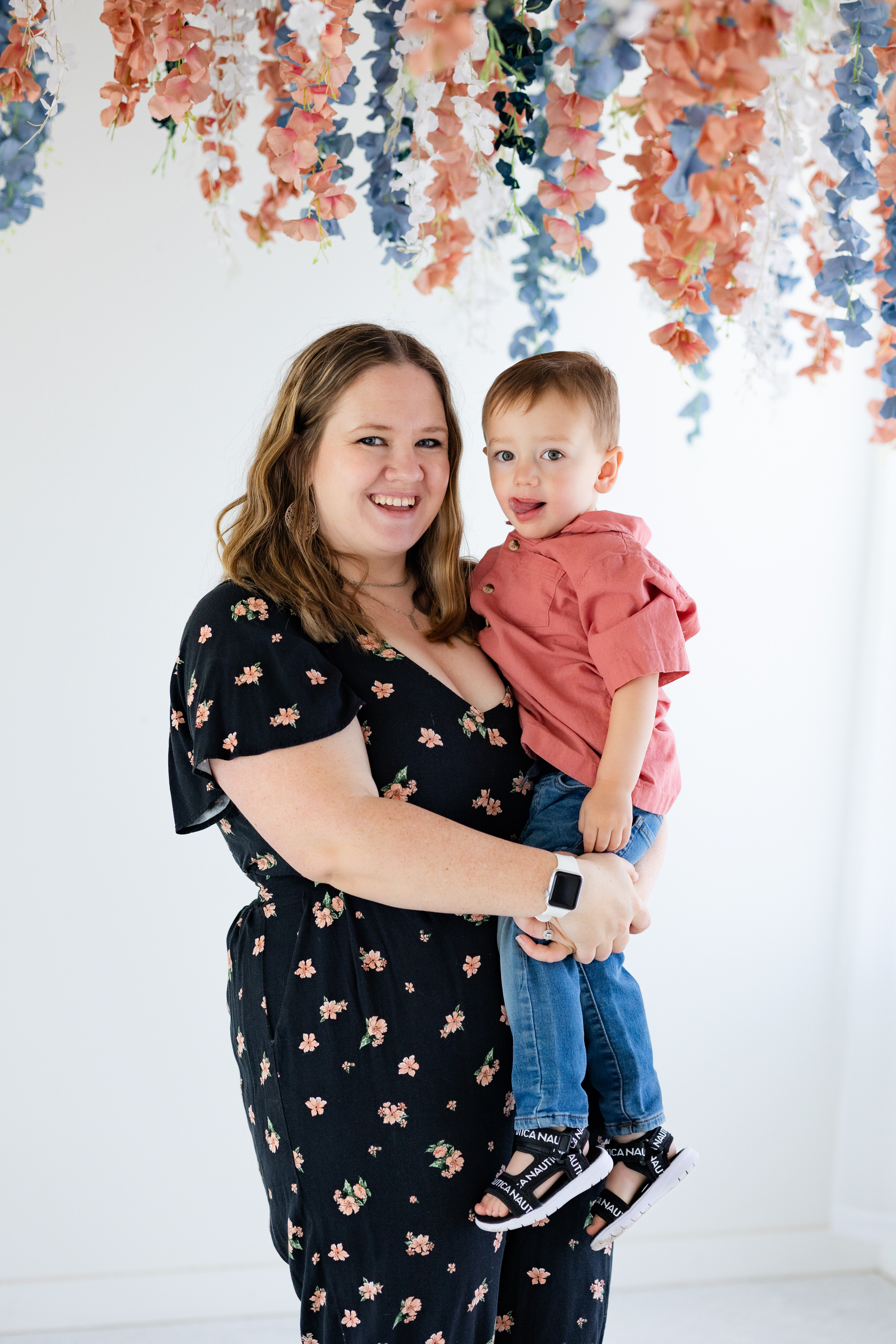 A mom holds her toddler son and smiles at the camera.
