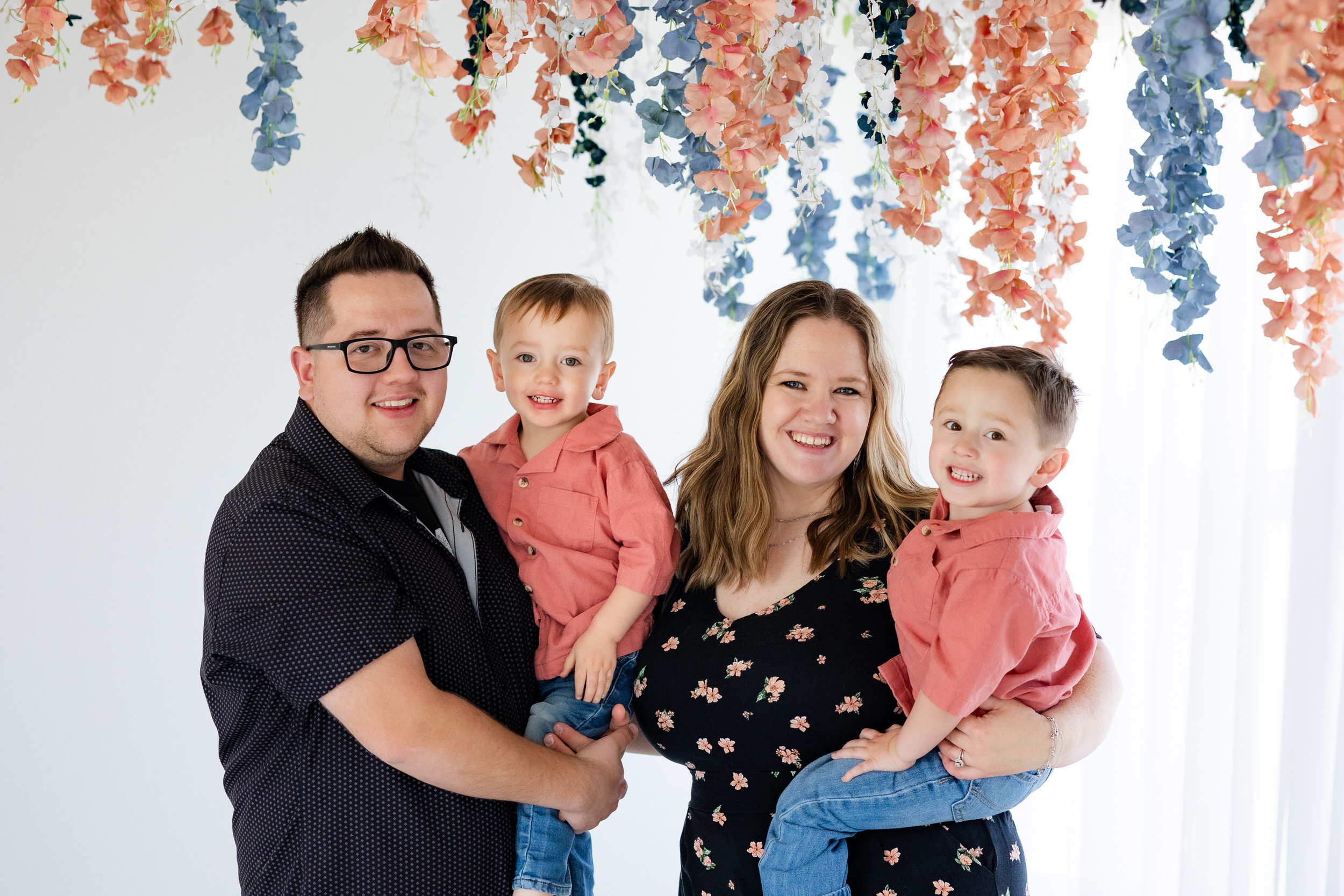 A mom and dad hold their two young boys and smile at the camera.