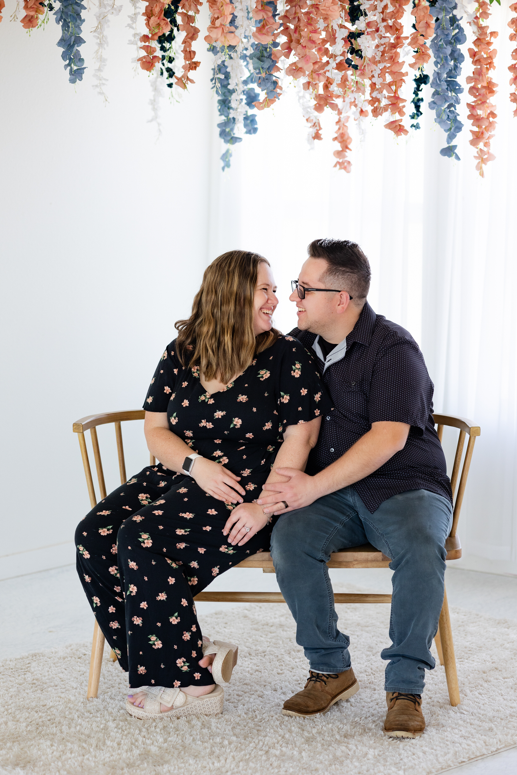 A husband and wife sit on a bench and smile at each other.