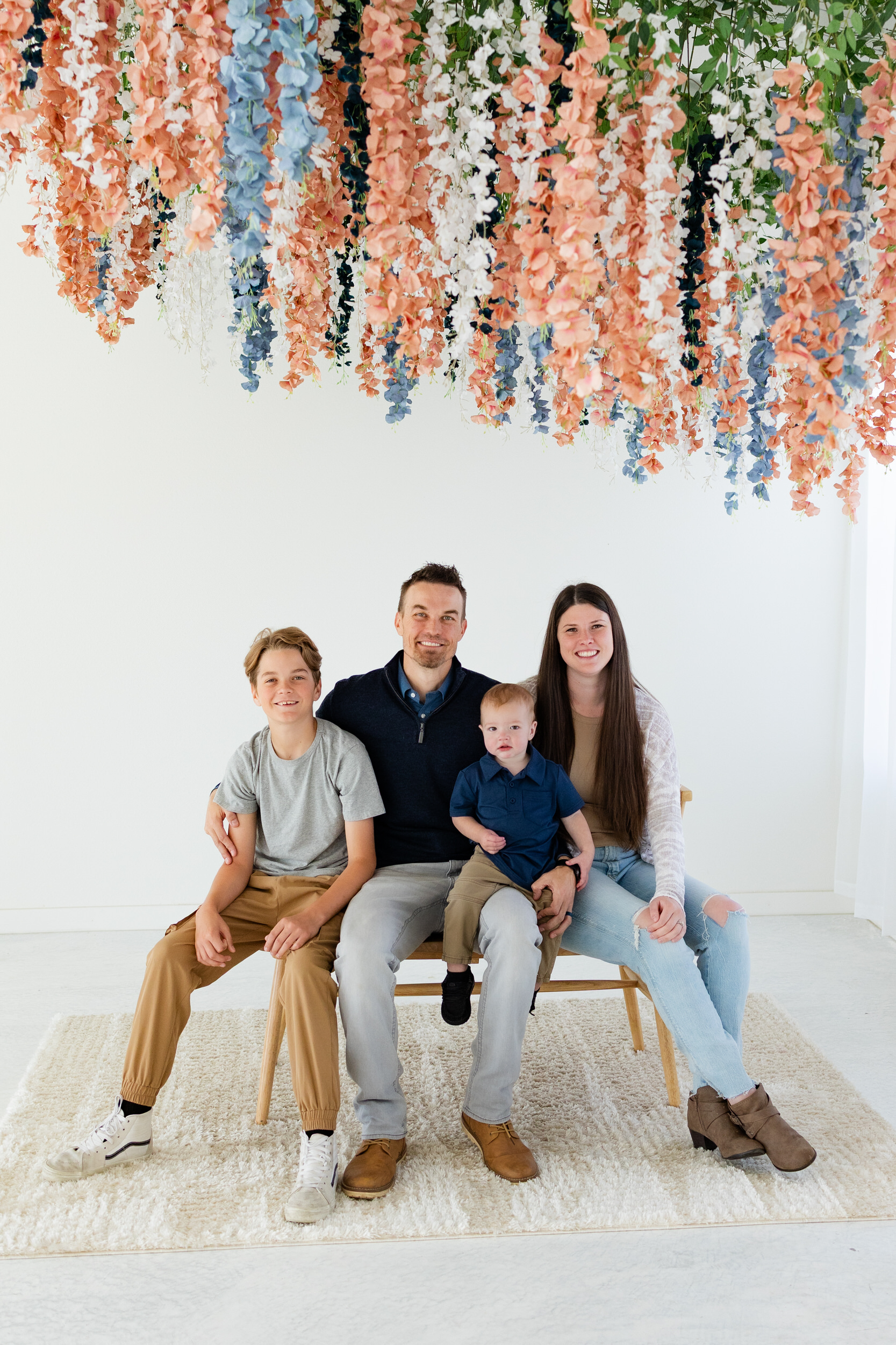 A family of four sits on a bench and smiles at the camera.
