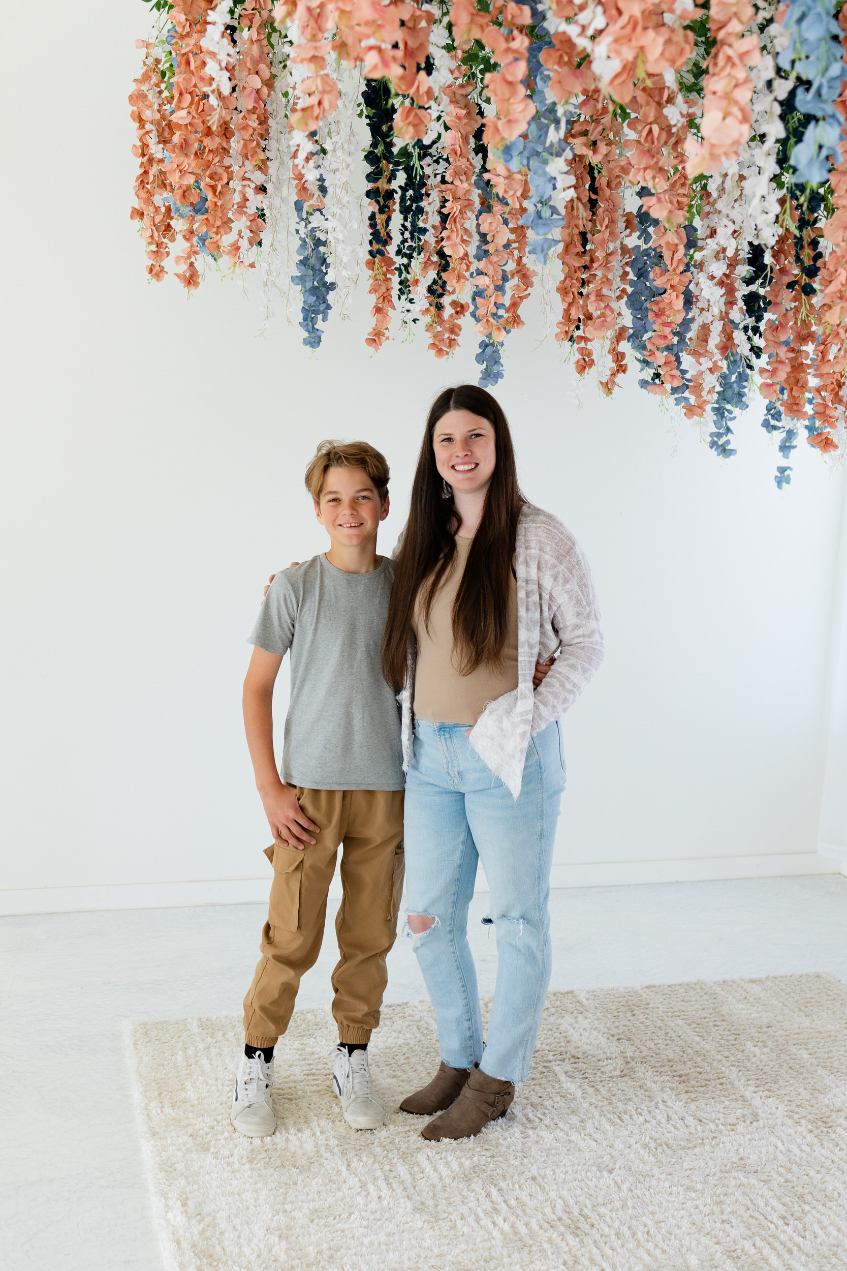A mom and her pre-teen son smile at the camera while standing next to each other with their arms around each other's shoulders.
