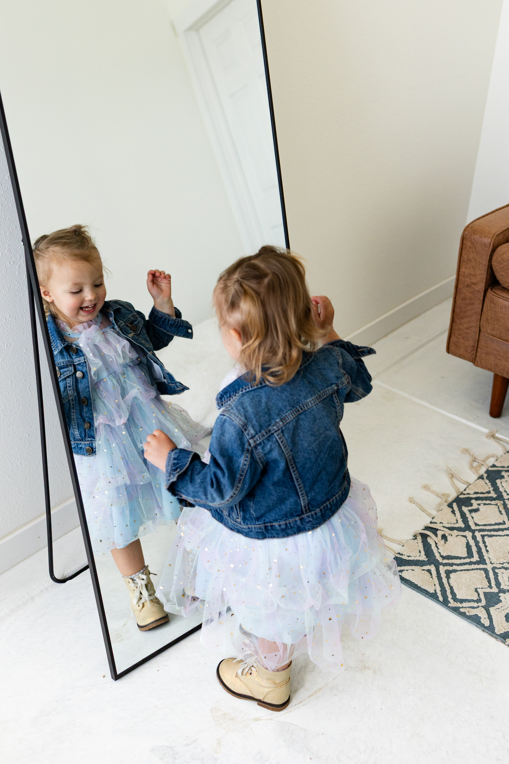 A little girl in a tulle dress looks in a mirror and smiles at herself.