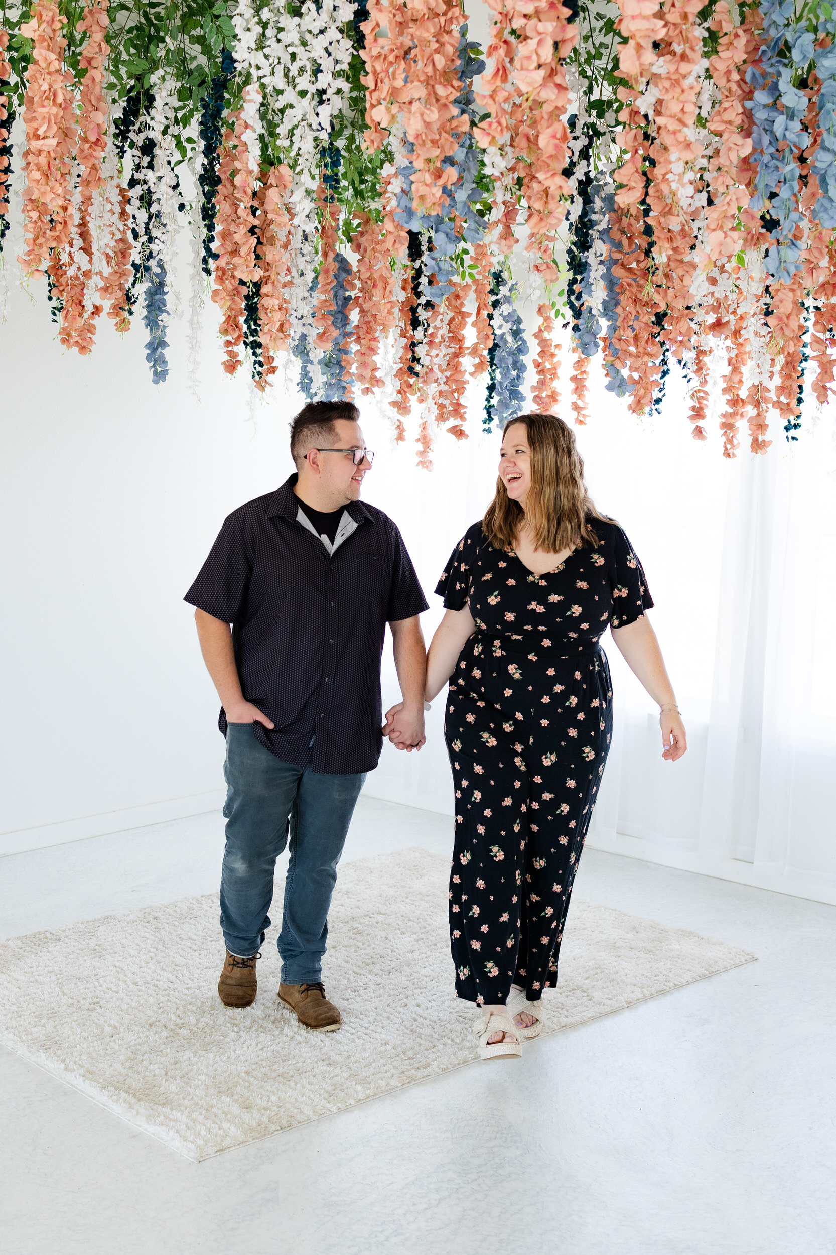 A husband and wife hold hands and smile at each other while walking toward the camera.