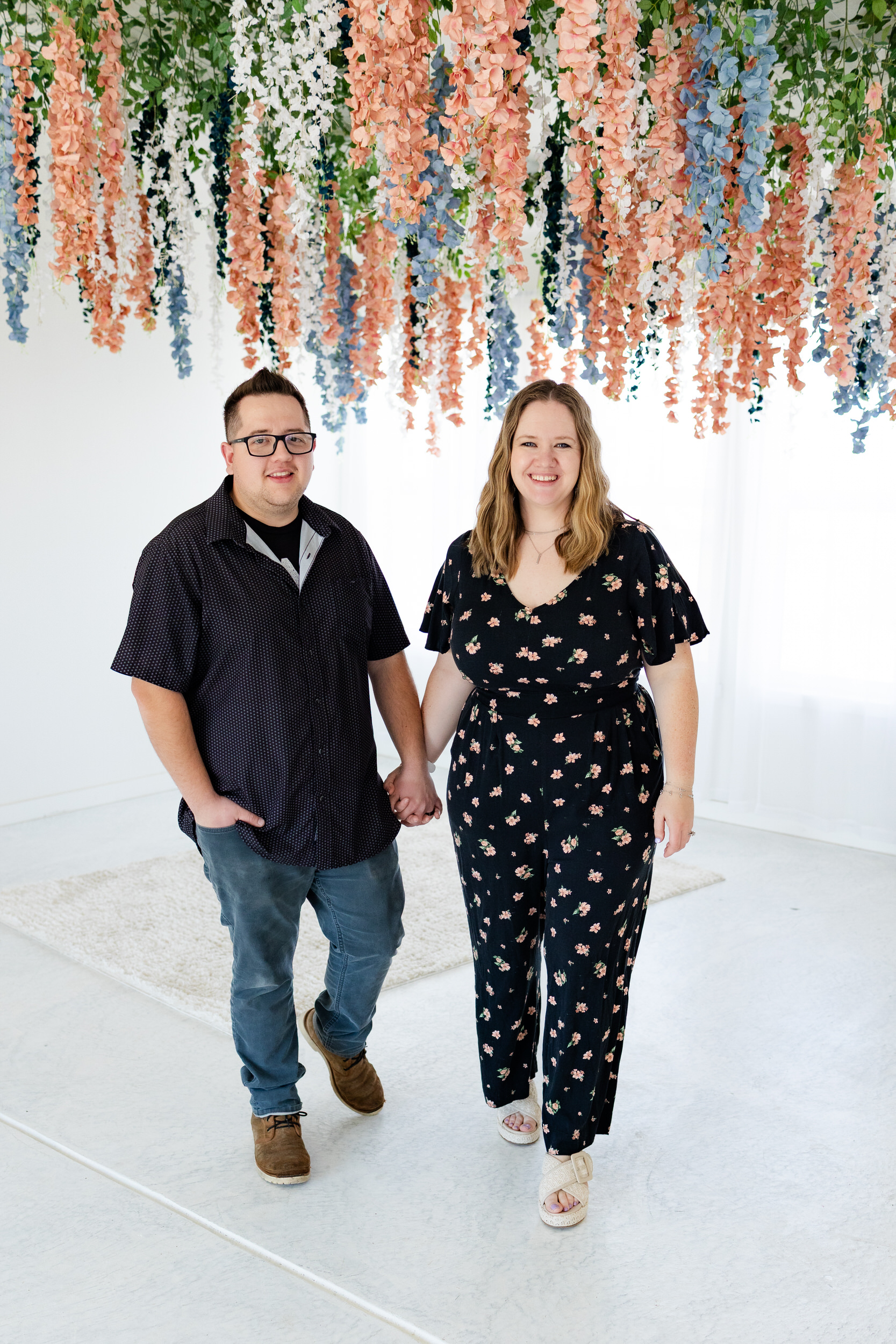 A husband and wife hold hands and walk toward the camera smiling.