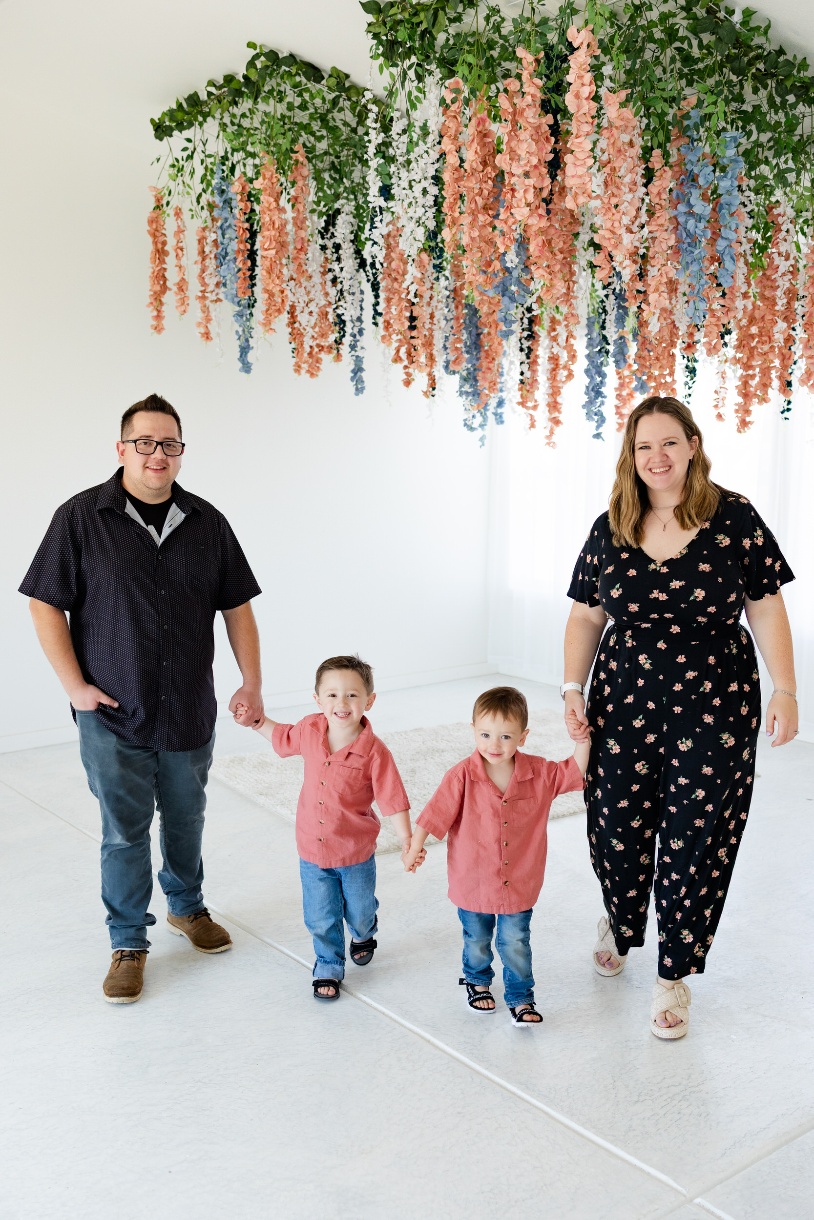 A family of four holds hands and walks toward the camera while smiling.