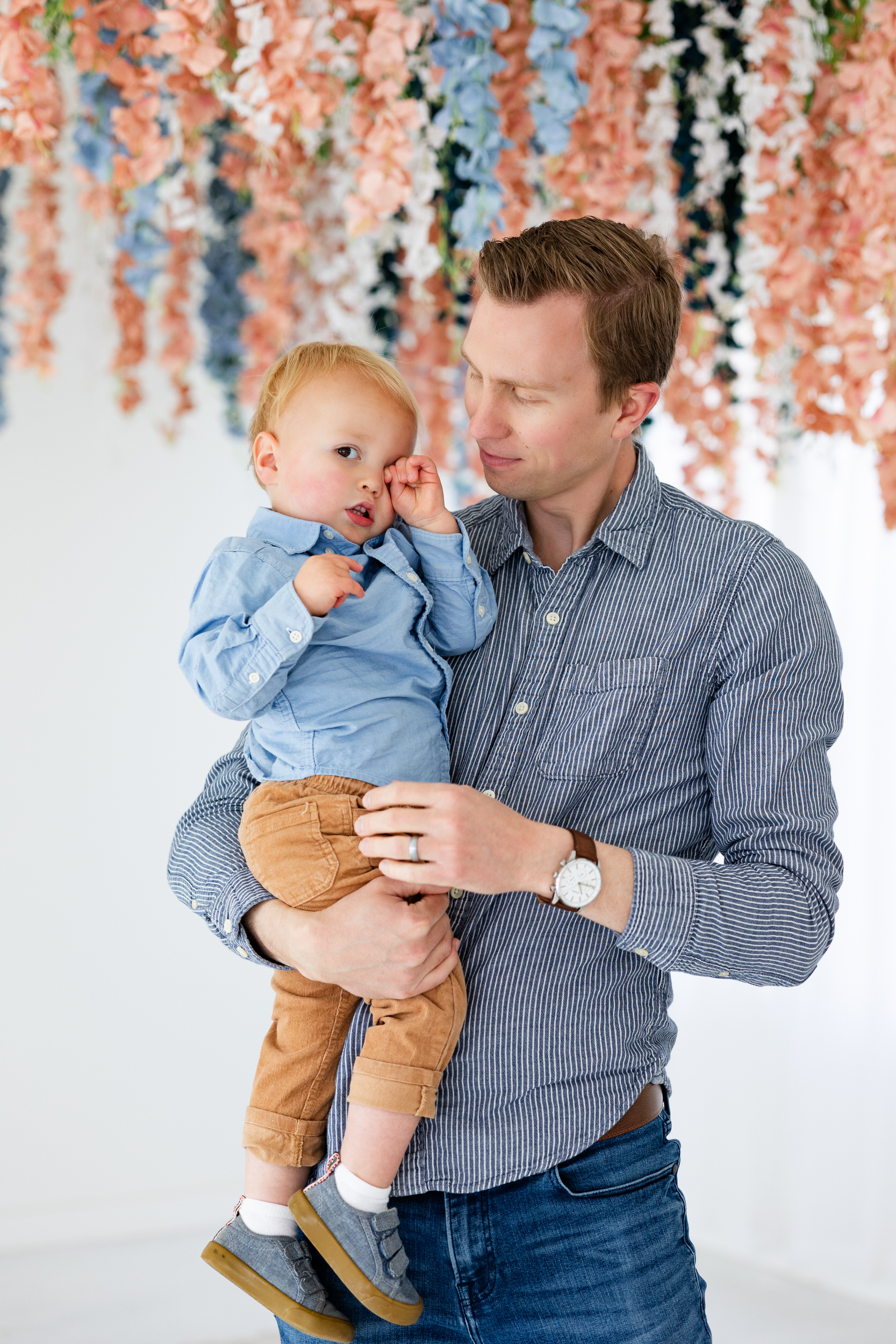 A dad holds his toddler son and smiles at him.