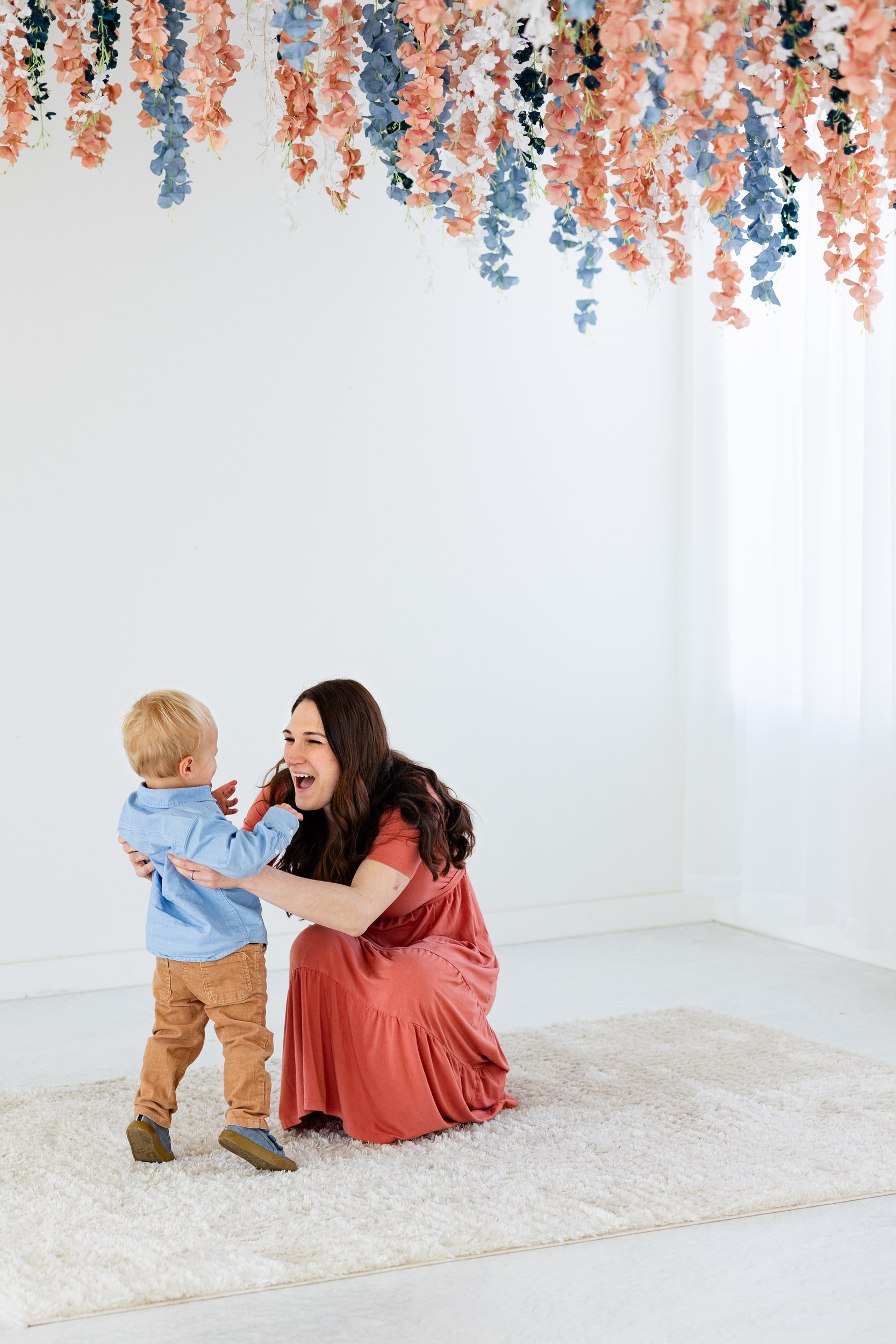 A mom squats down to hug her toddler son.