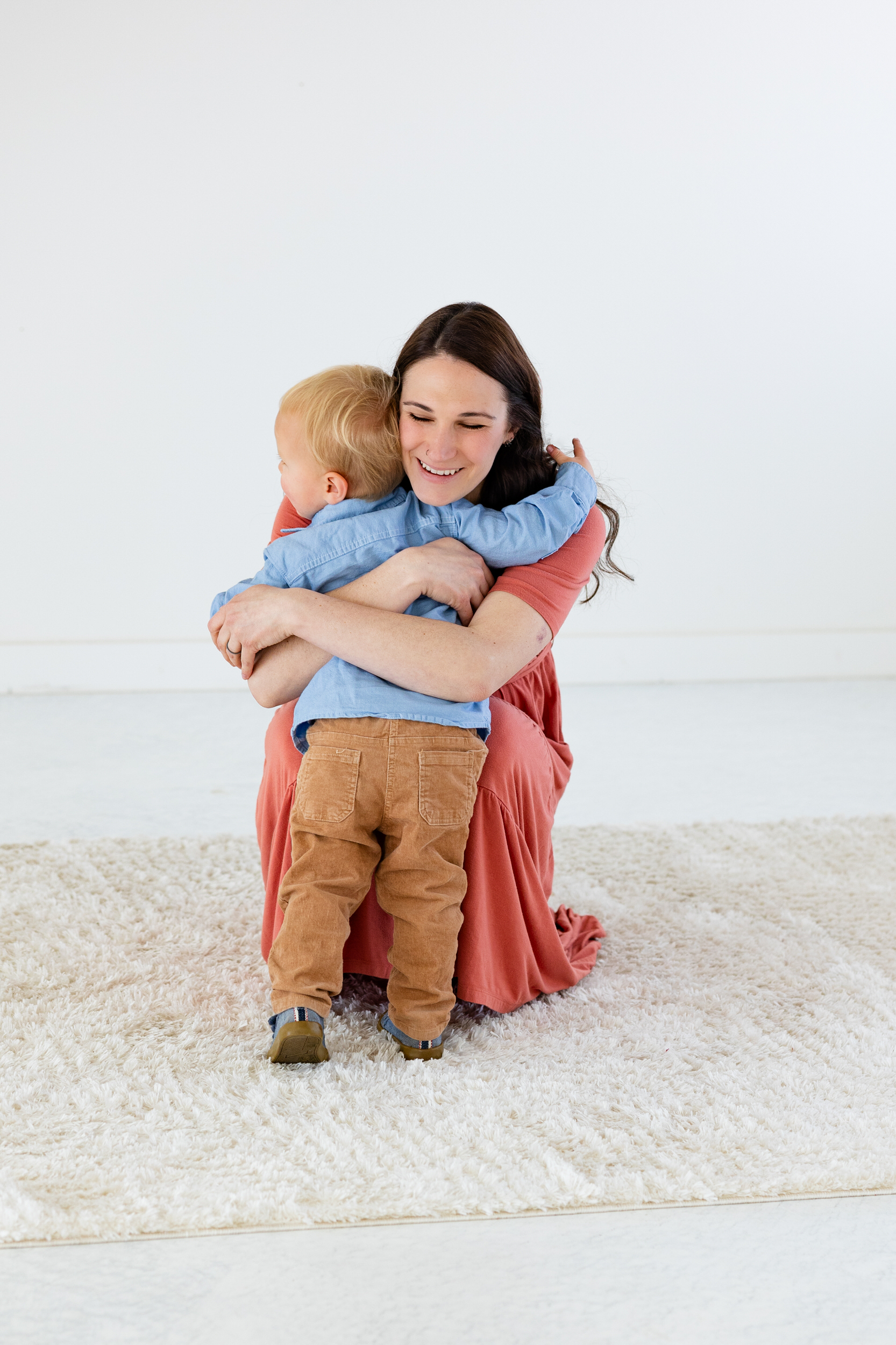 A mom squats down and hugs her toddler son.