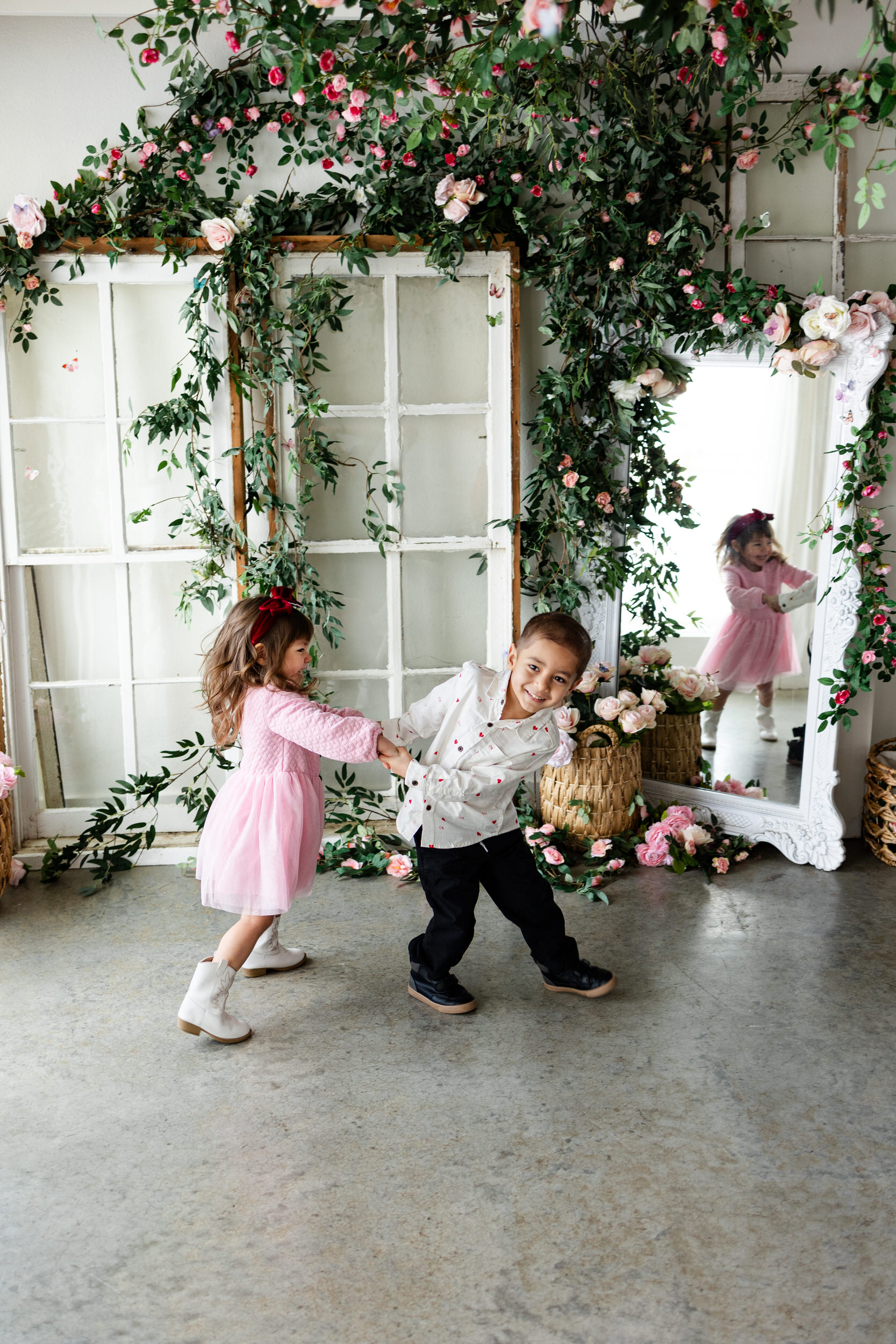 A young brother and sister hold hands and spin around while laughing together.