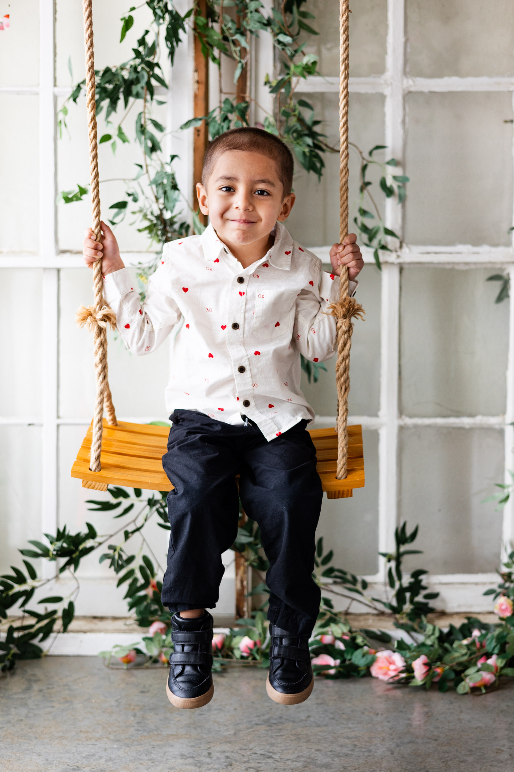 A little boy smiles while sitting on a wooden swing.