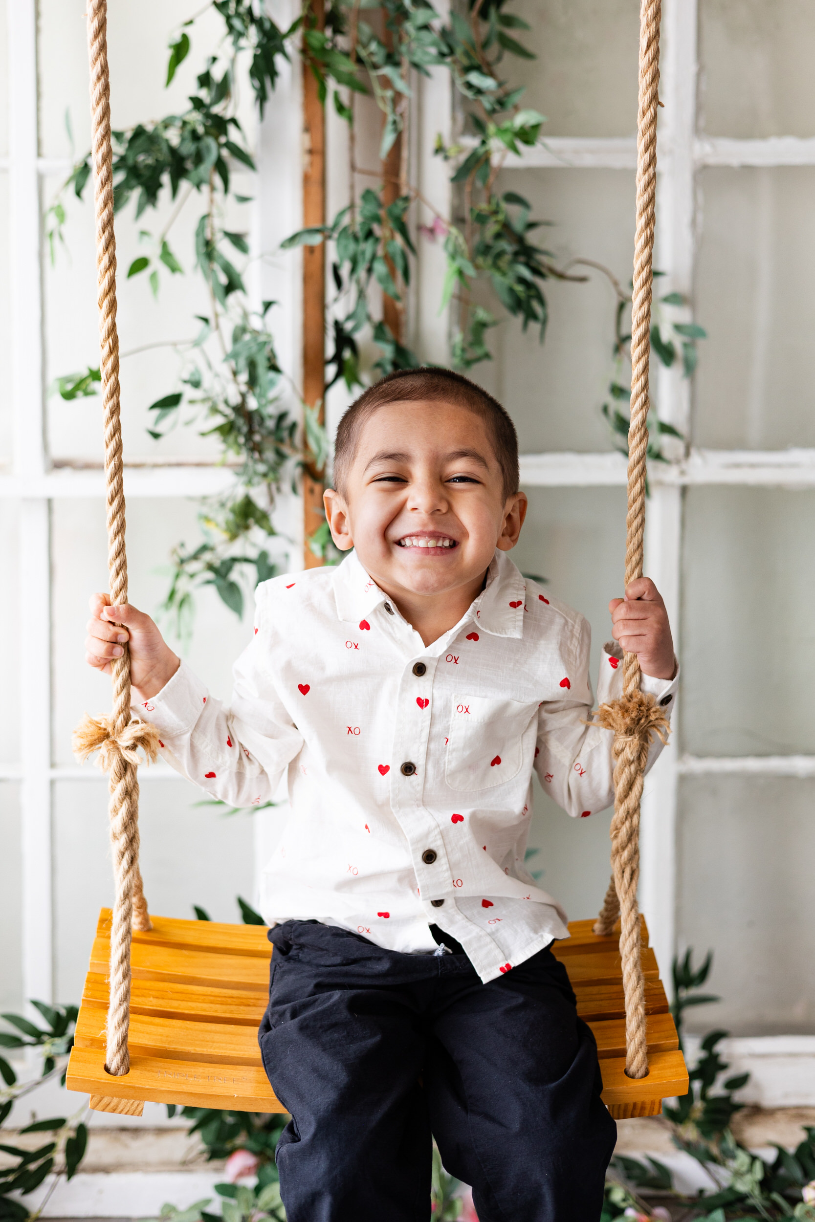 A little boy smiles while sitting on a wooden swing.