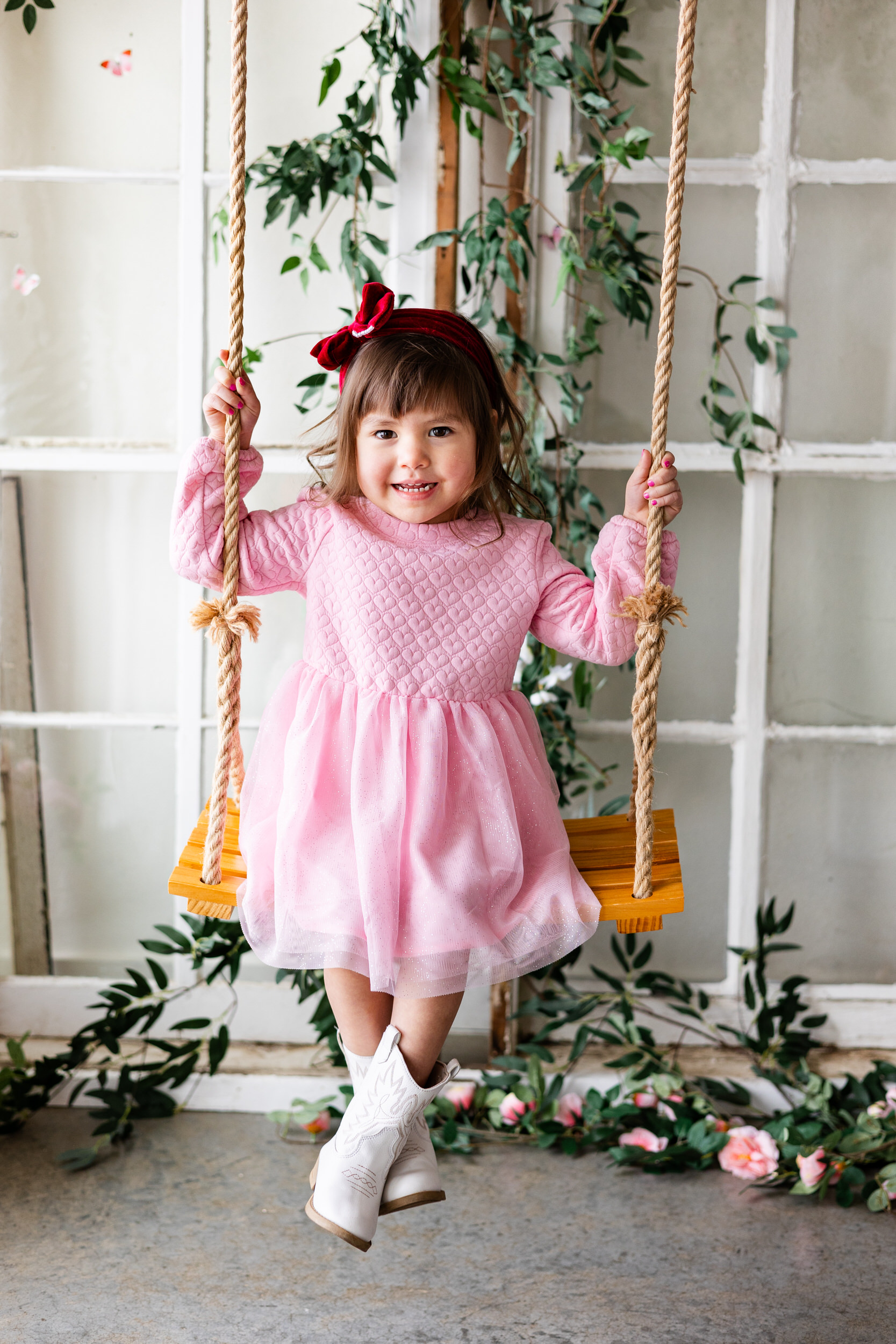 A little girl smiles while sitting on a wooden swing.