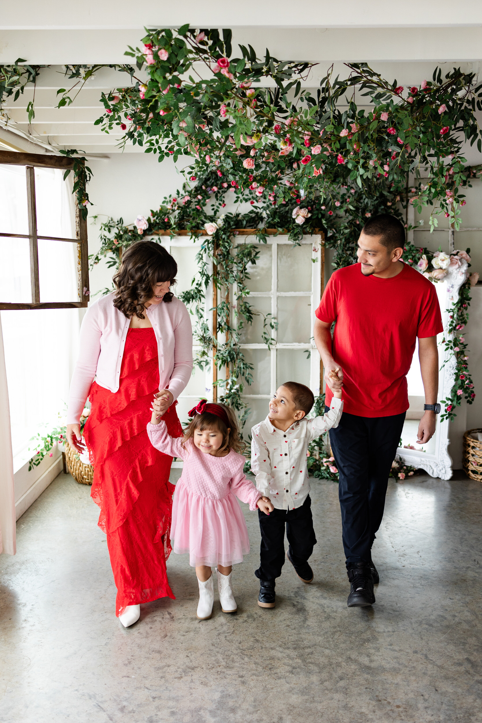 A family of four holds hands while walking toward the camera and looking at each other.