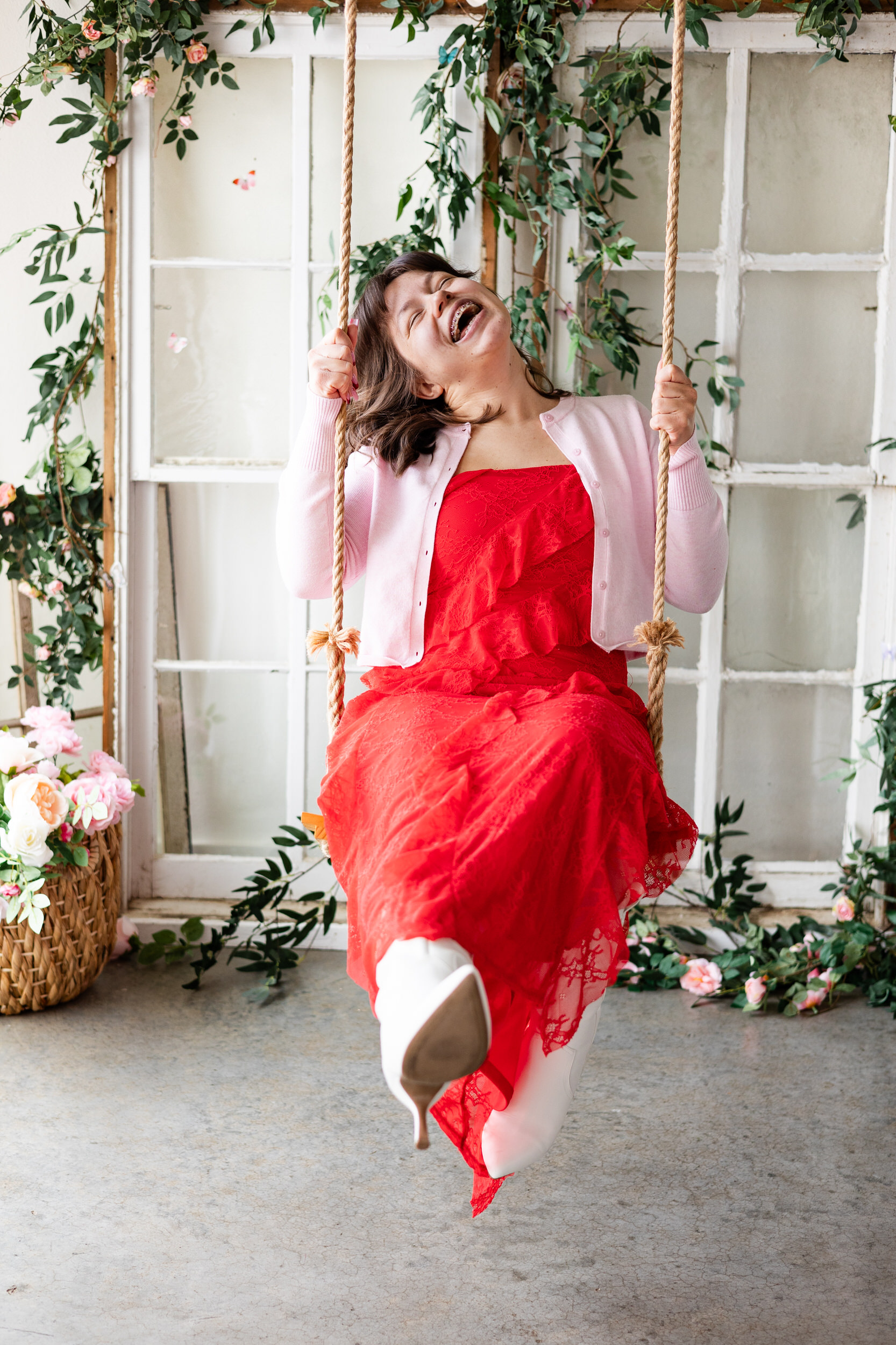A woman in a red dress sits on a wooden swing and throws her head back as she laughs.