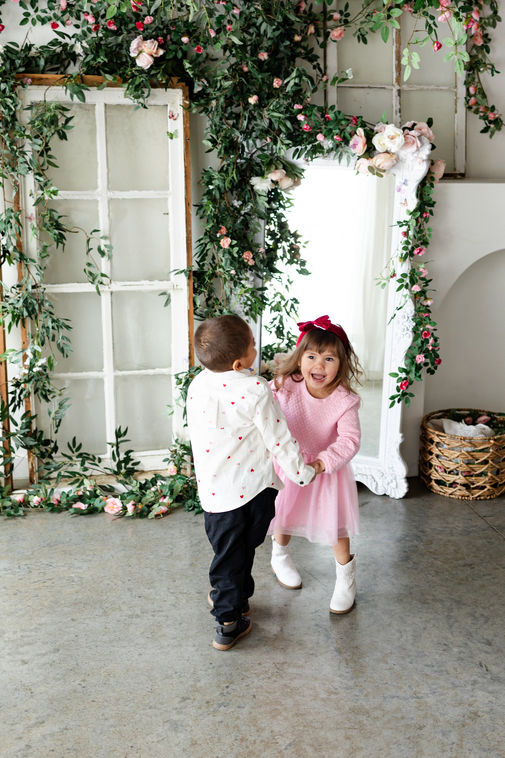 A brother and sister hold hands and spin around while laughing together.