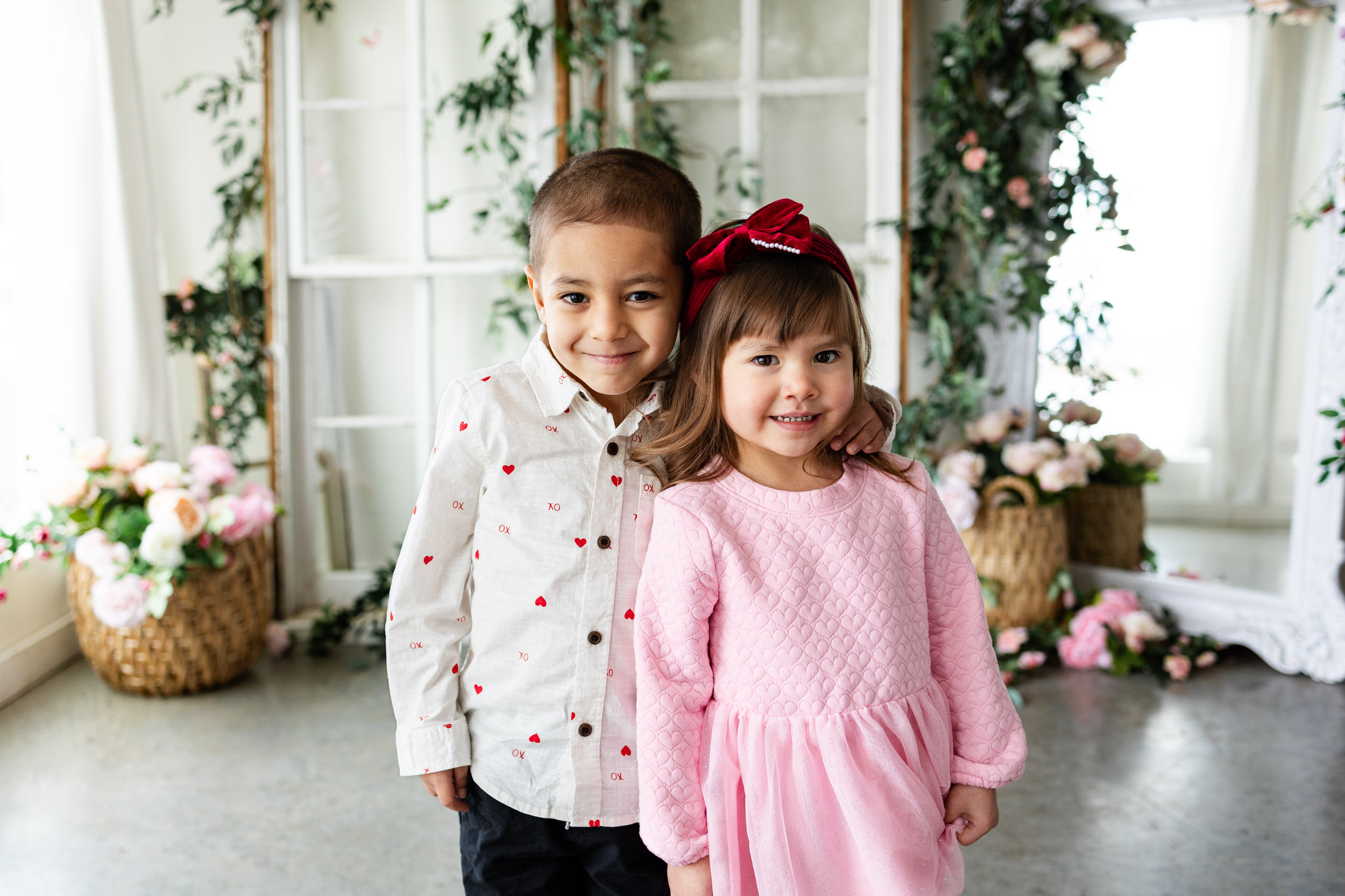 A young brother and sister smile at the camera with their arms around each other's shoulders.