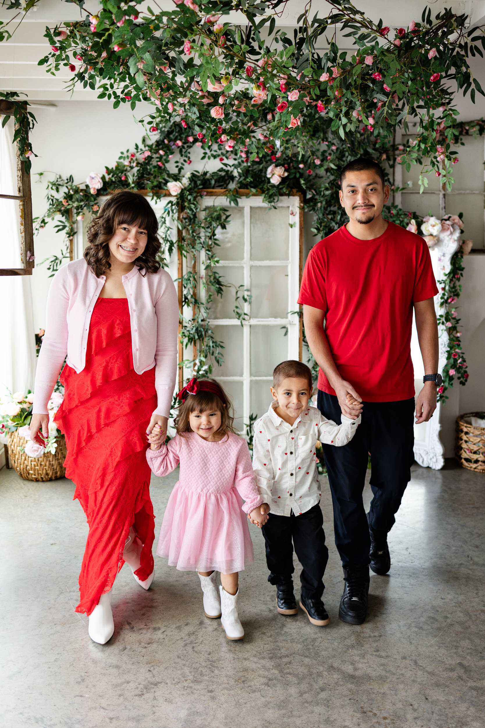 A family of four walks toward the camera and smiles in a studio filled with flowers.