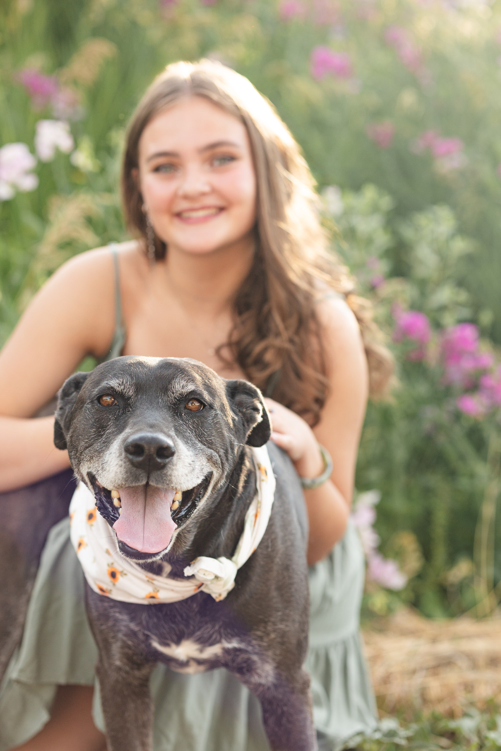 A dog "smiles" at the camera while a woman hugs the dog and smiles in the background.