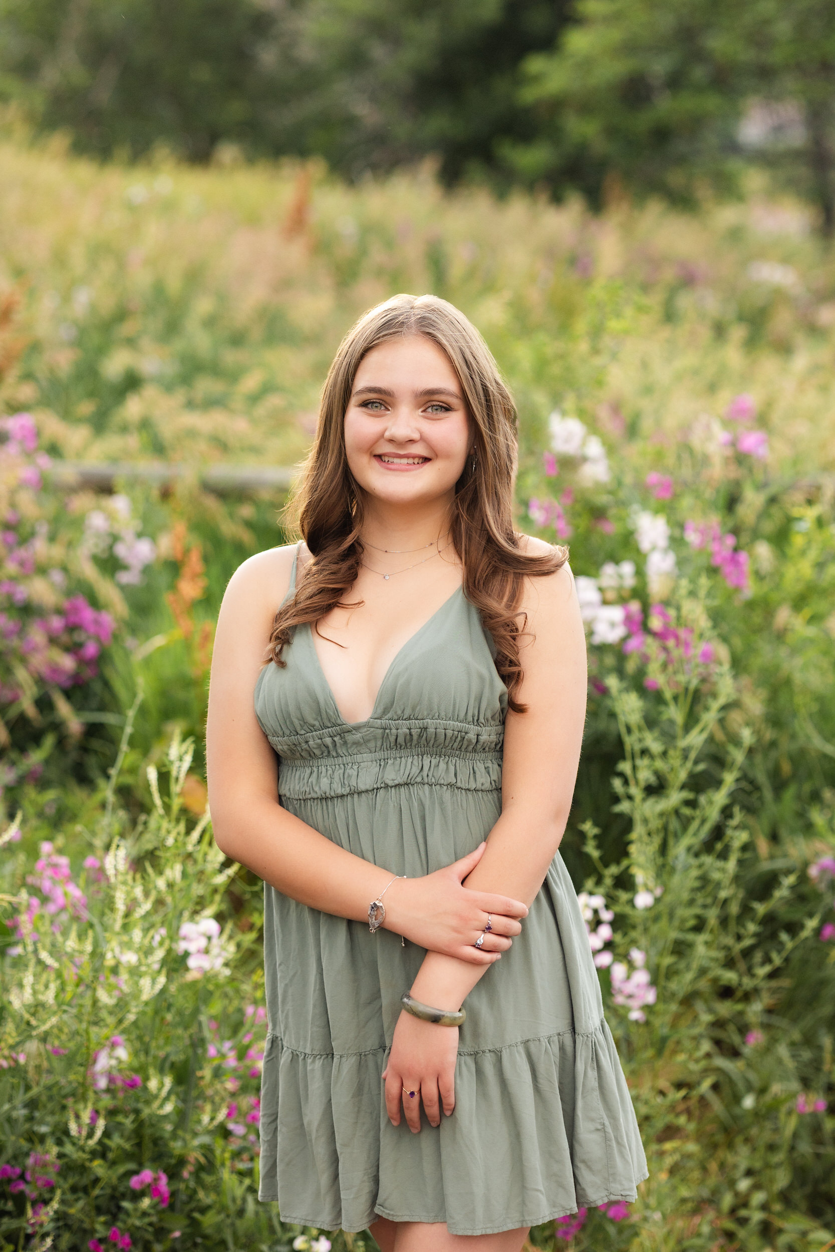A young woman in a green surrounded by wildflowers smiles at the camera.