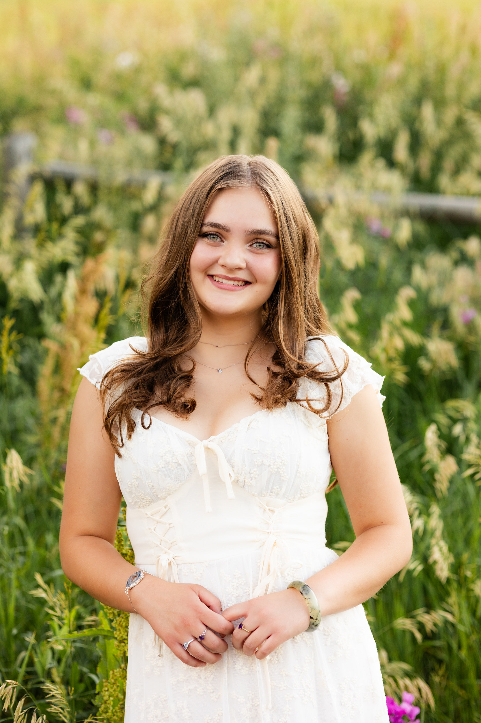 A woman in a white dress surrounded by wildflowers smiles at the camera.