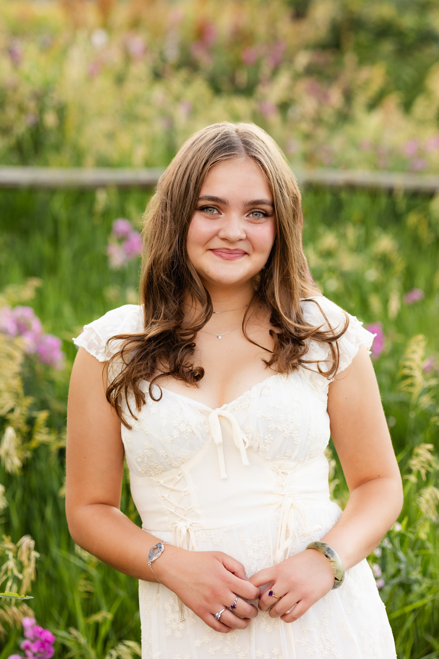A woman in a white dress surrounded by wildflowers smiles at the camera.