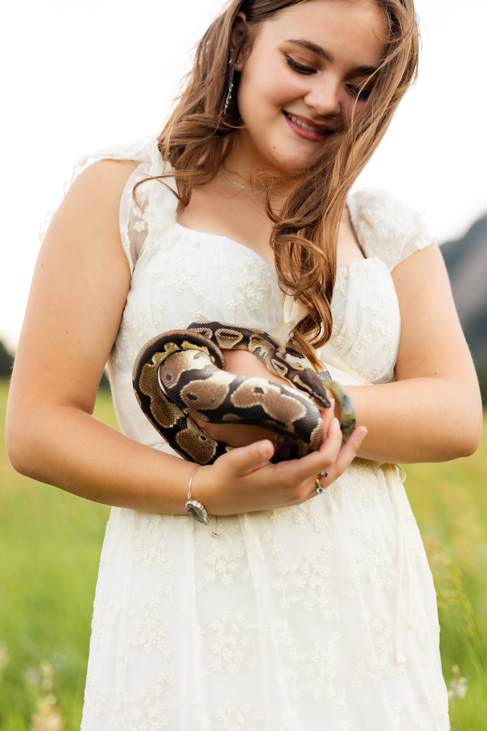 A woman in a white dress standing in a field holds her snake.