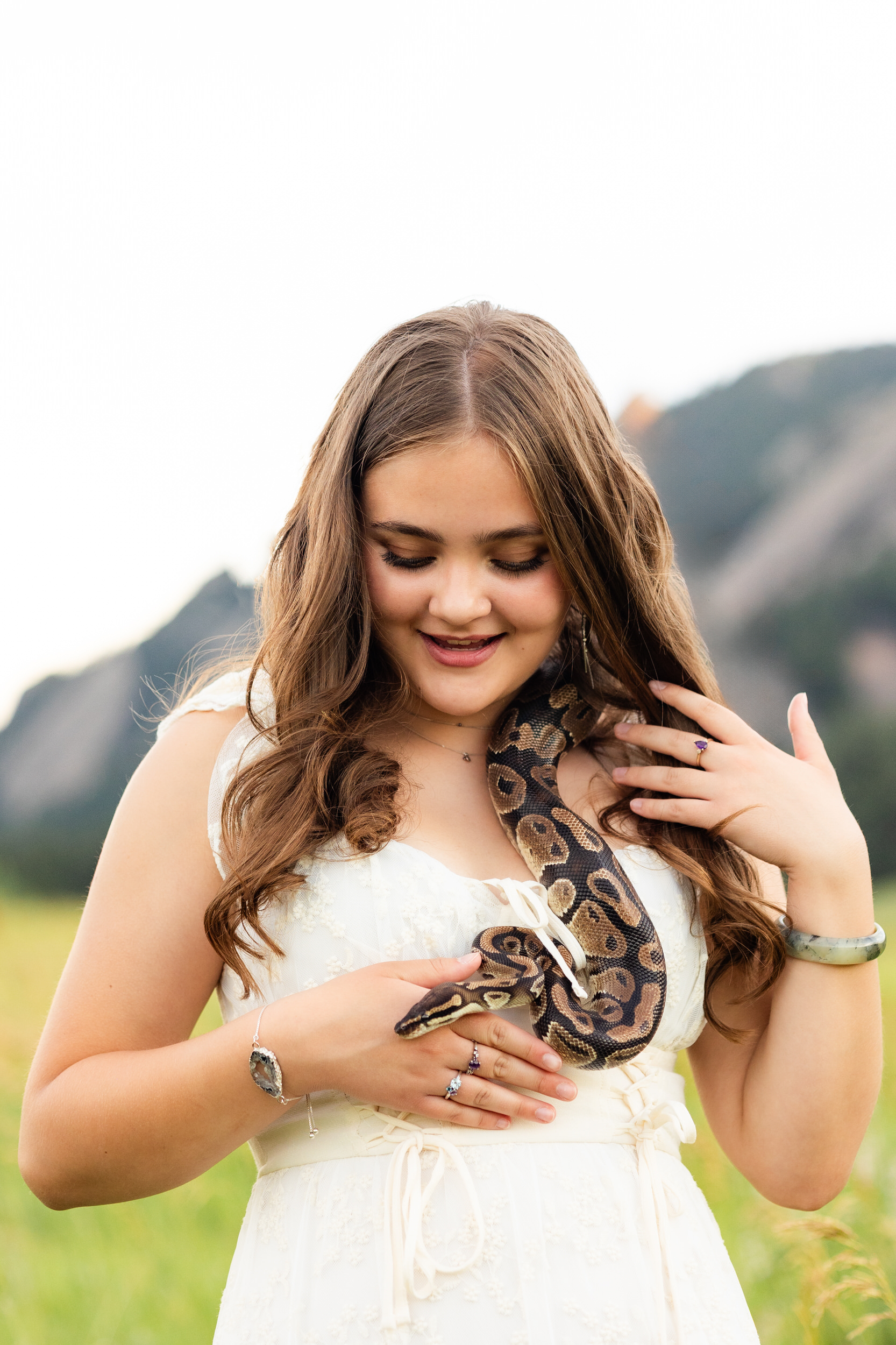 A woman in a white dress smiles at a snake that slithering over her shoulder.