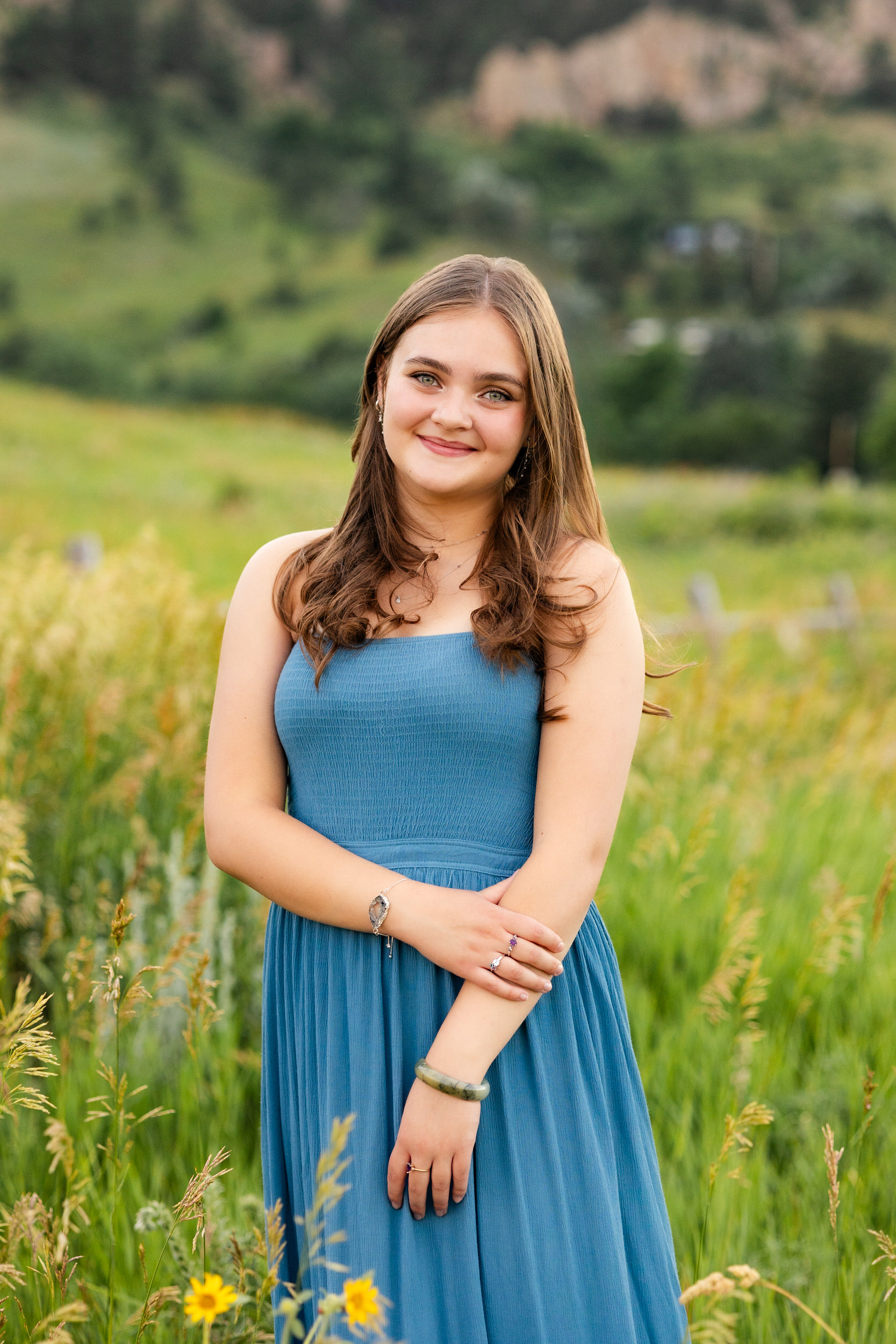A woman in a teal dress stands in a field and smiles at the camera.