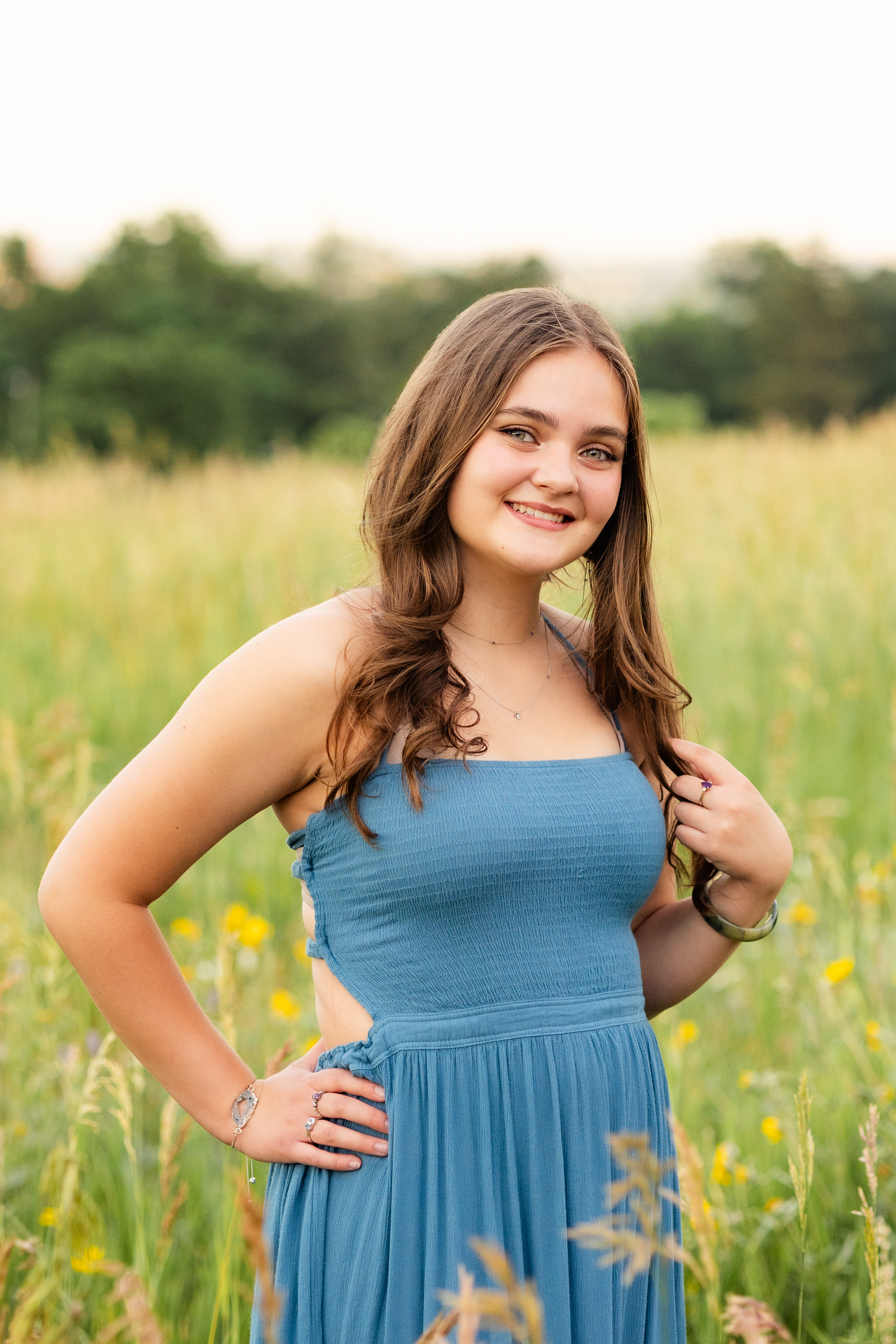 A woman in a teal dress stands in a field and smiles at the camera.