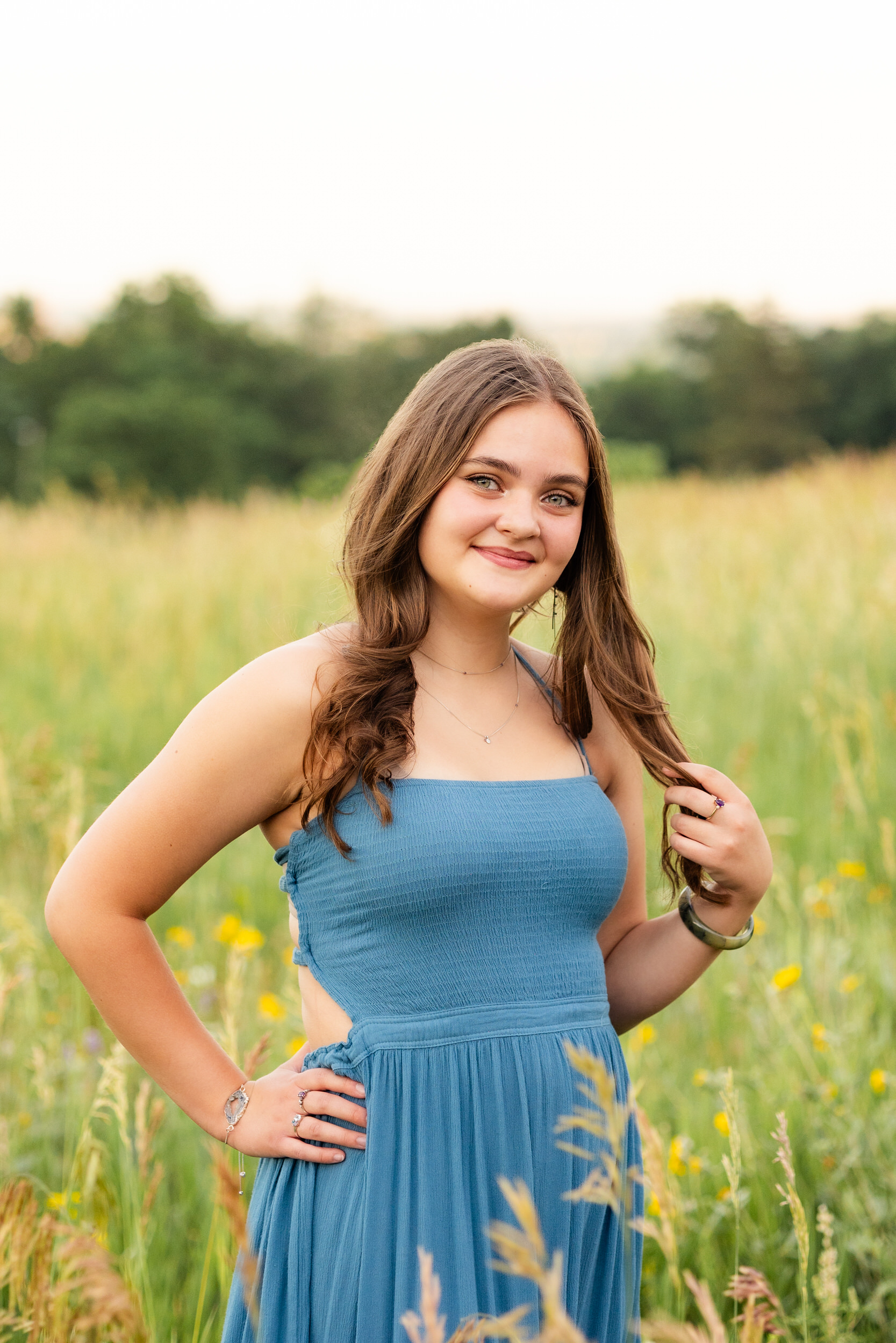 A woman in a teal dress stands in a field and smiles at the camera.