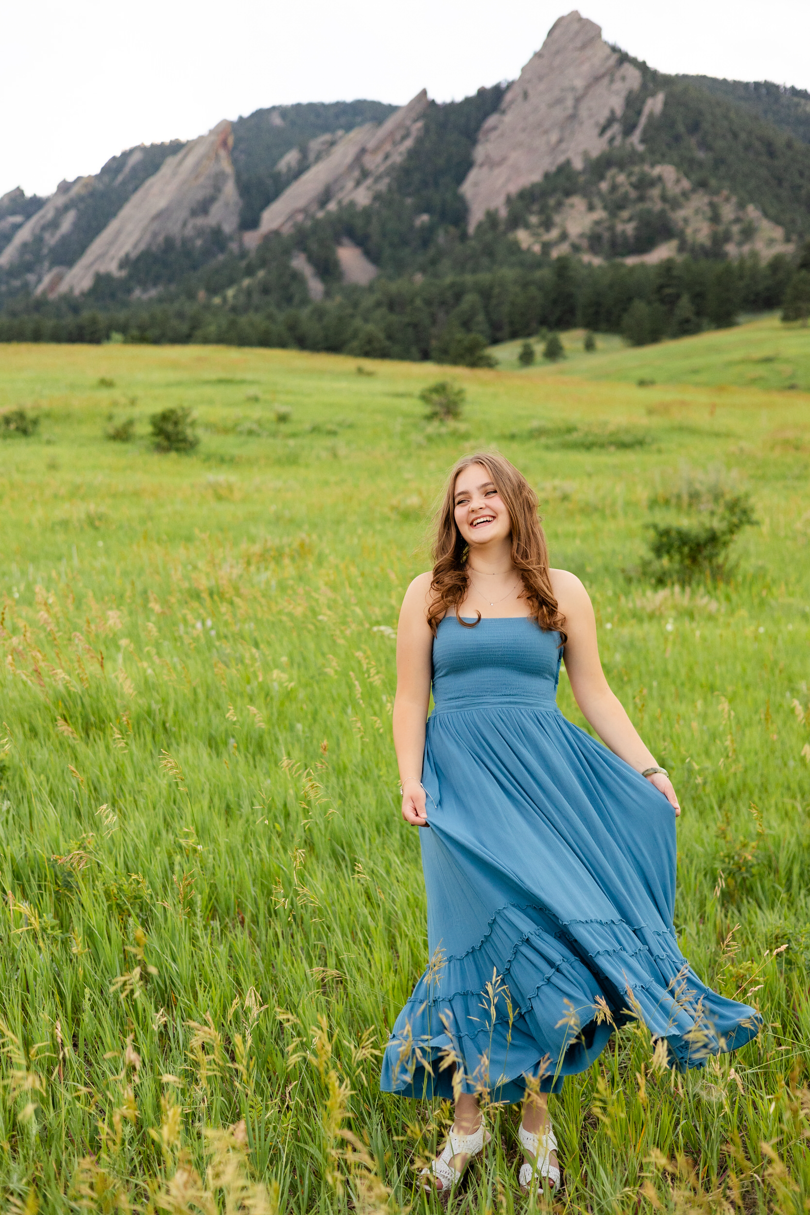 A woman in a teal dress swishes her skirt in a field and laughs.