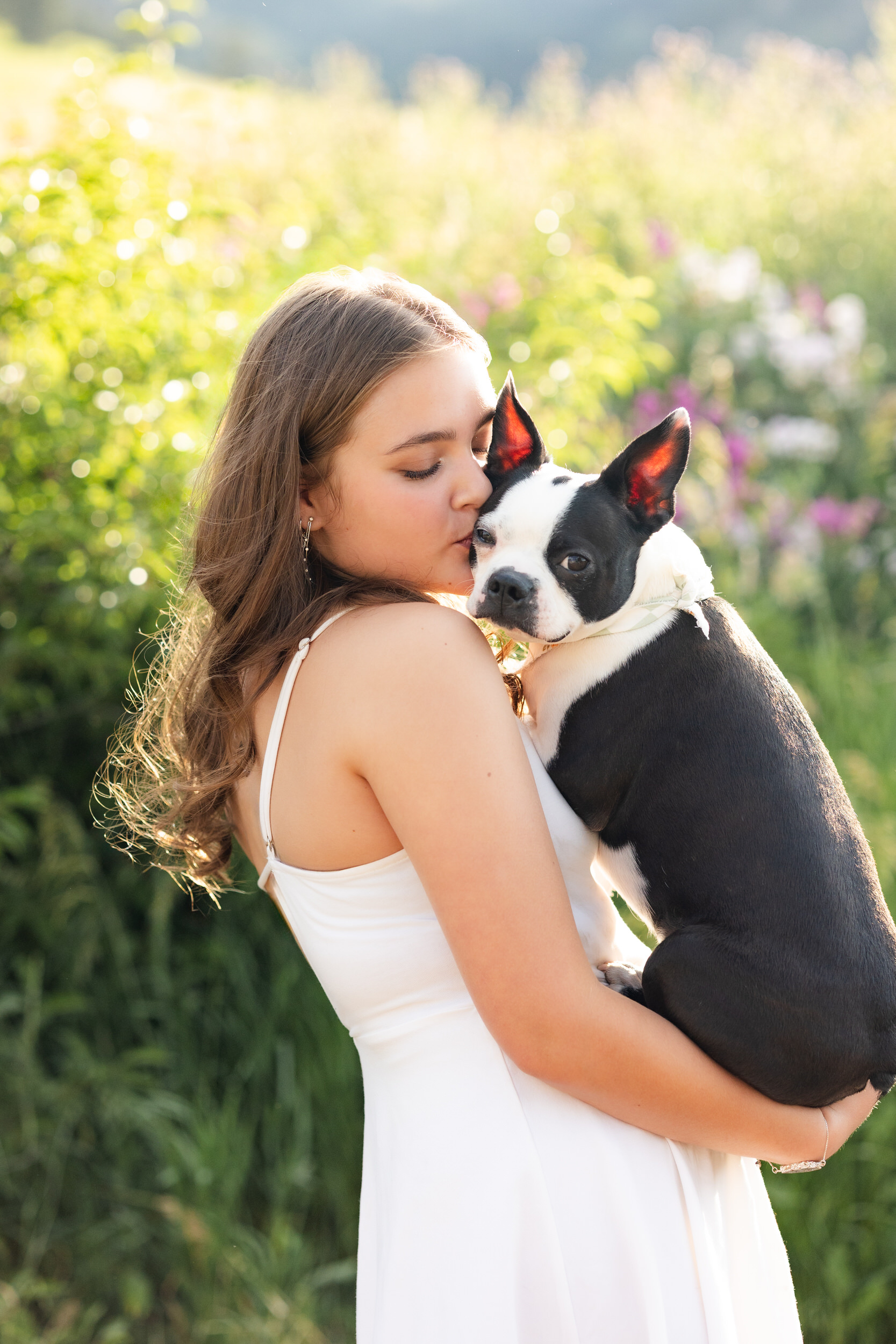 A woman holds a French Bulldog and gives him a kiss on the head.