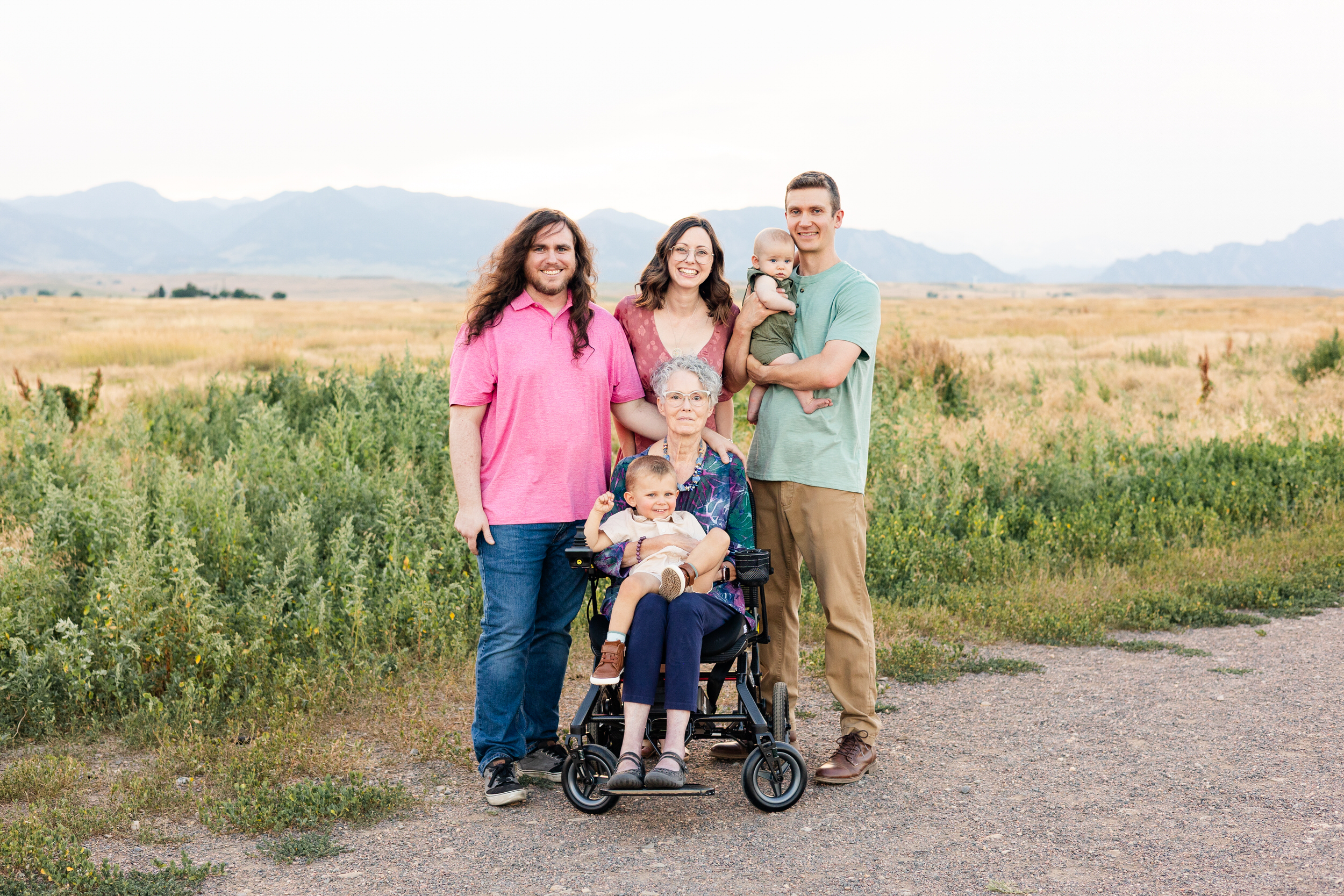 Woman sits in wheelchair with her grandson in her lap and the rest of the family gathers around her and smiles.