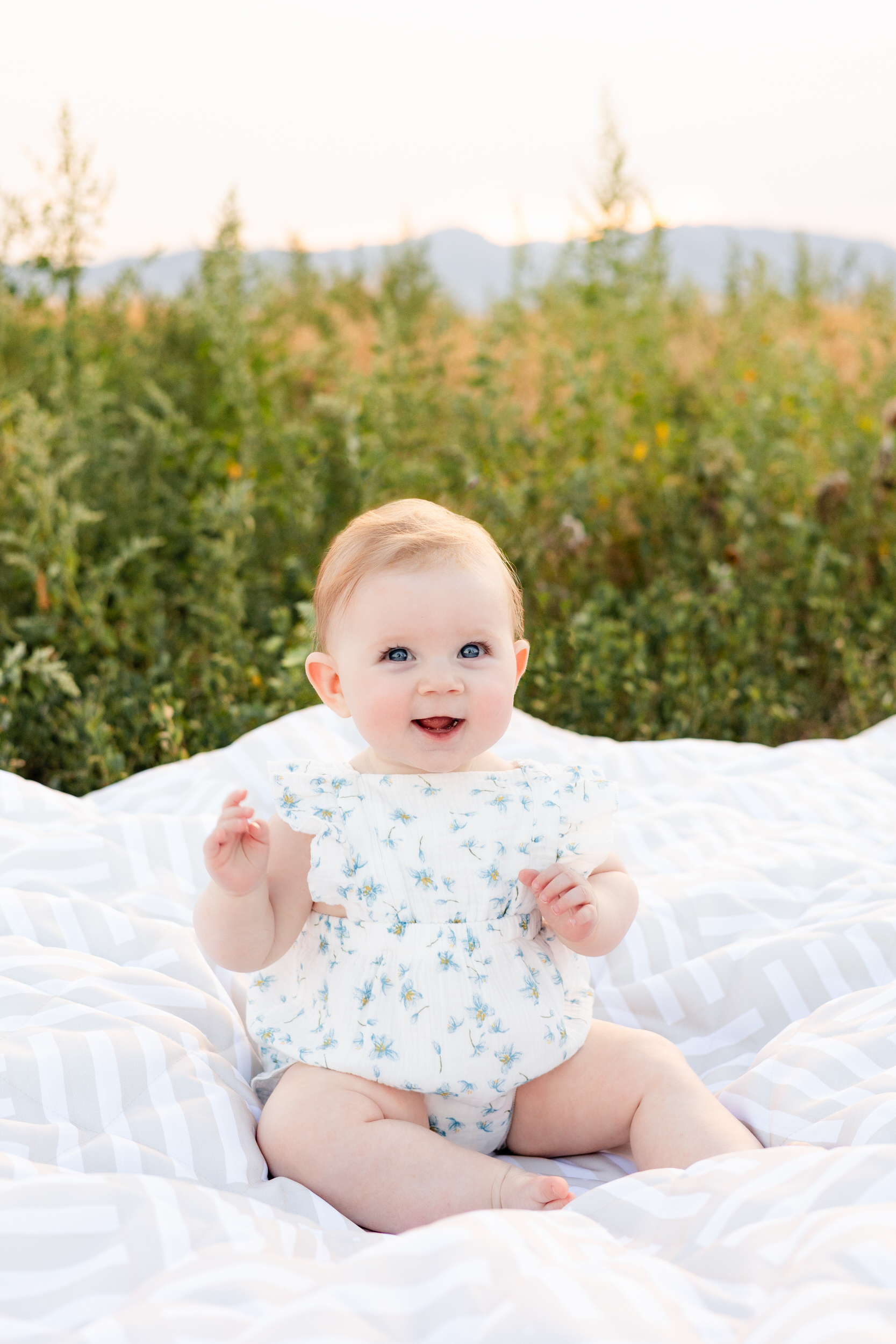 Baby girl smiles while sitting on blanket.
