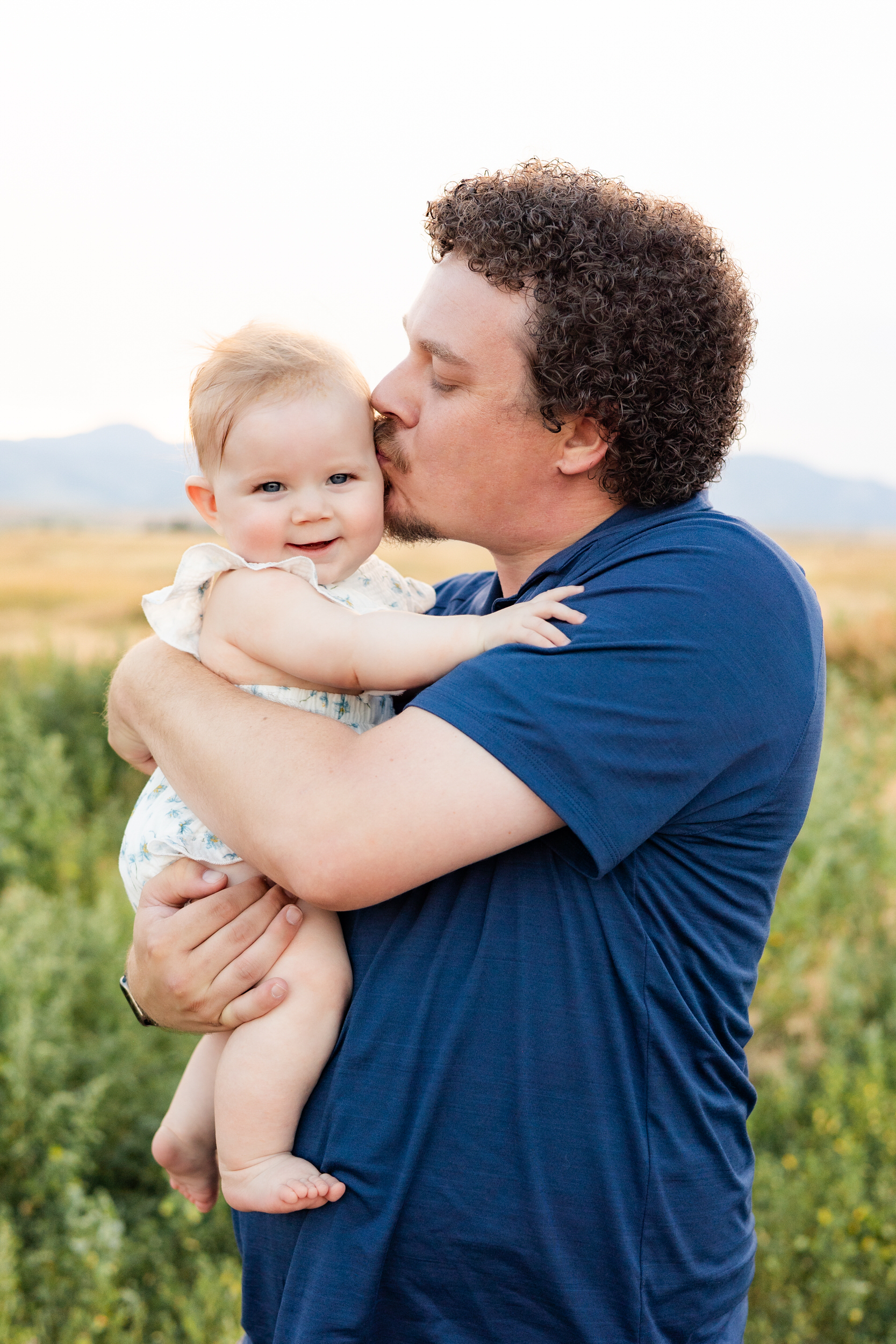 Dad kisses baby girl on her head.