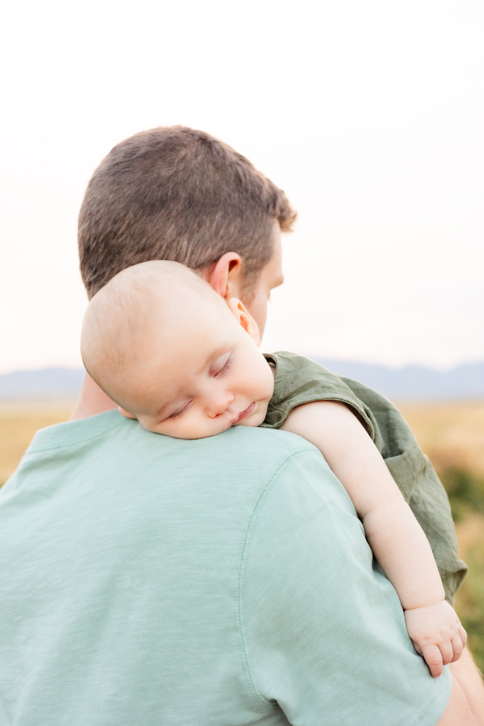 Baby boy sleeps on dad's shoulder.