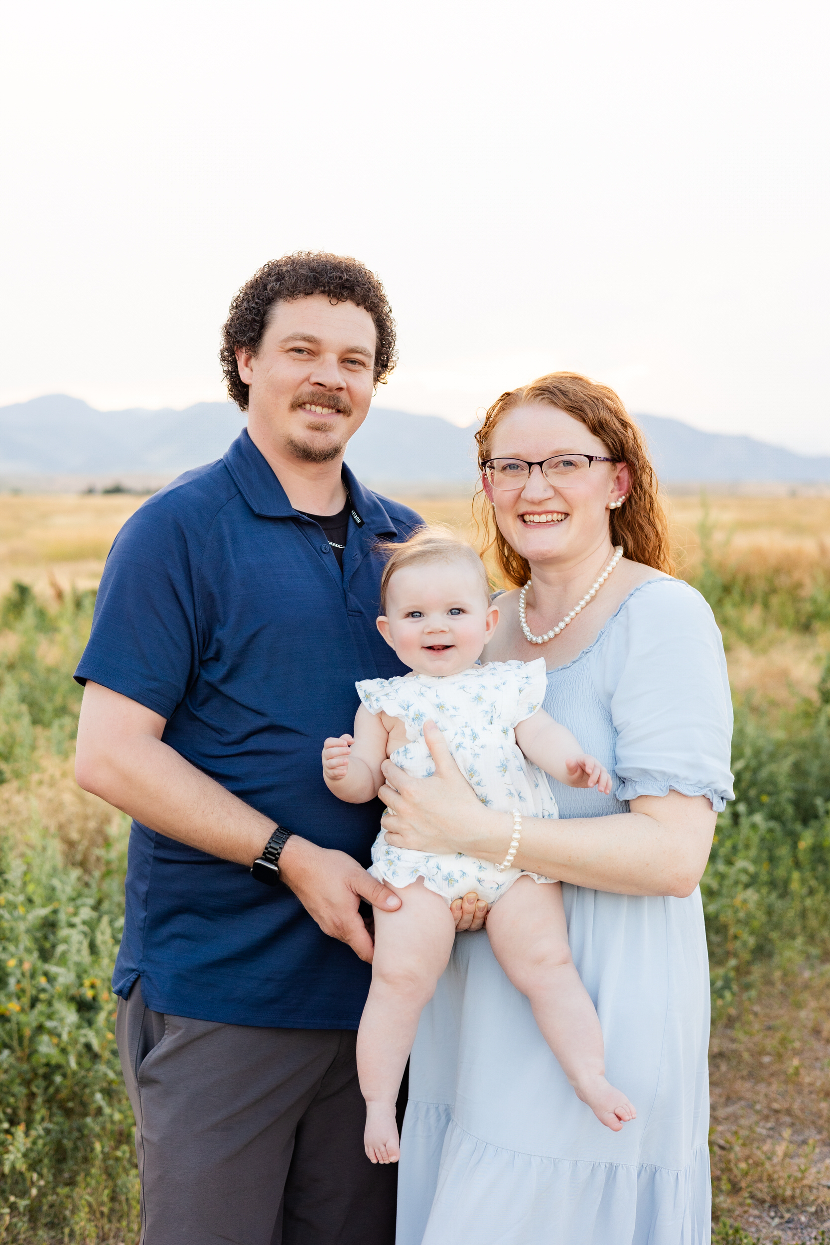 Mom, dad, and baby girl smile at the camera.