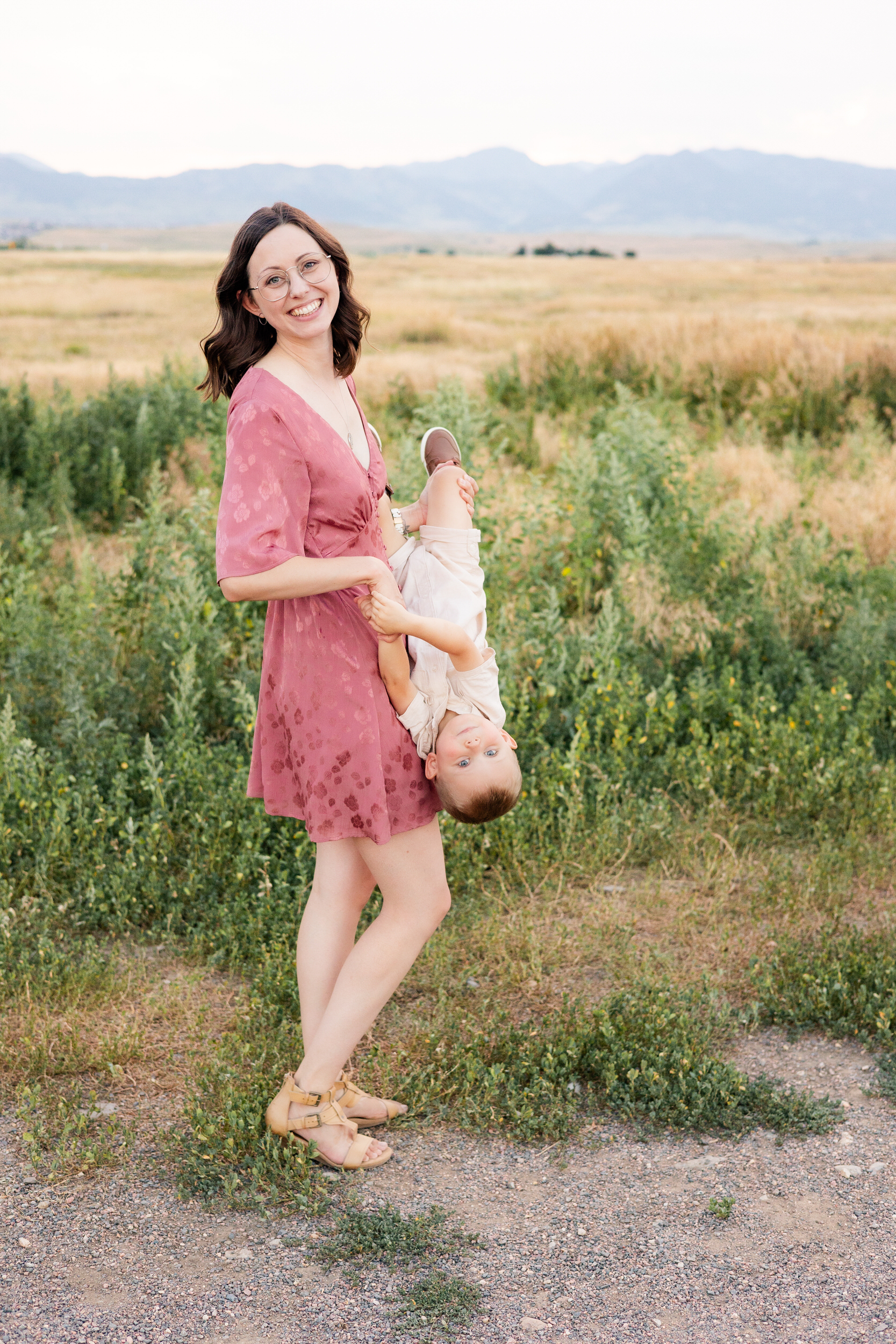 Mom holds young son upside down and they smile at the camera.