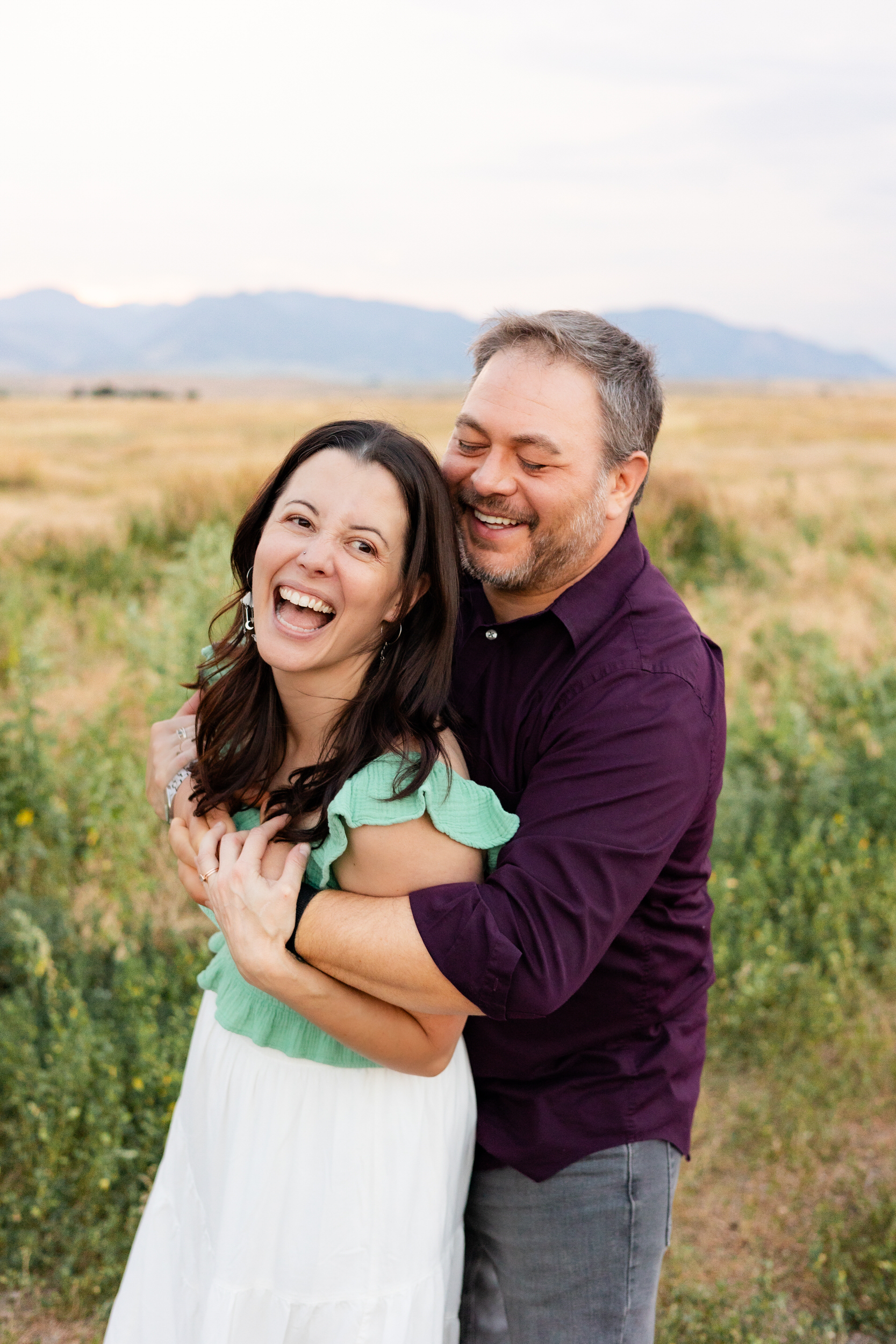 Husband hugs wife around shoulders as she laughs.