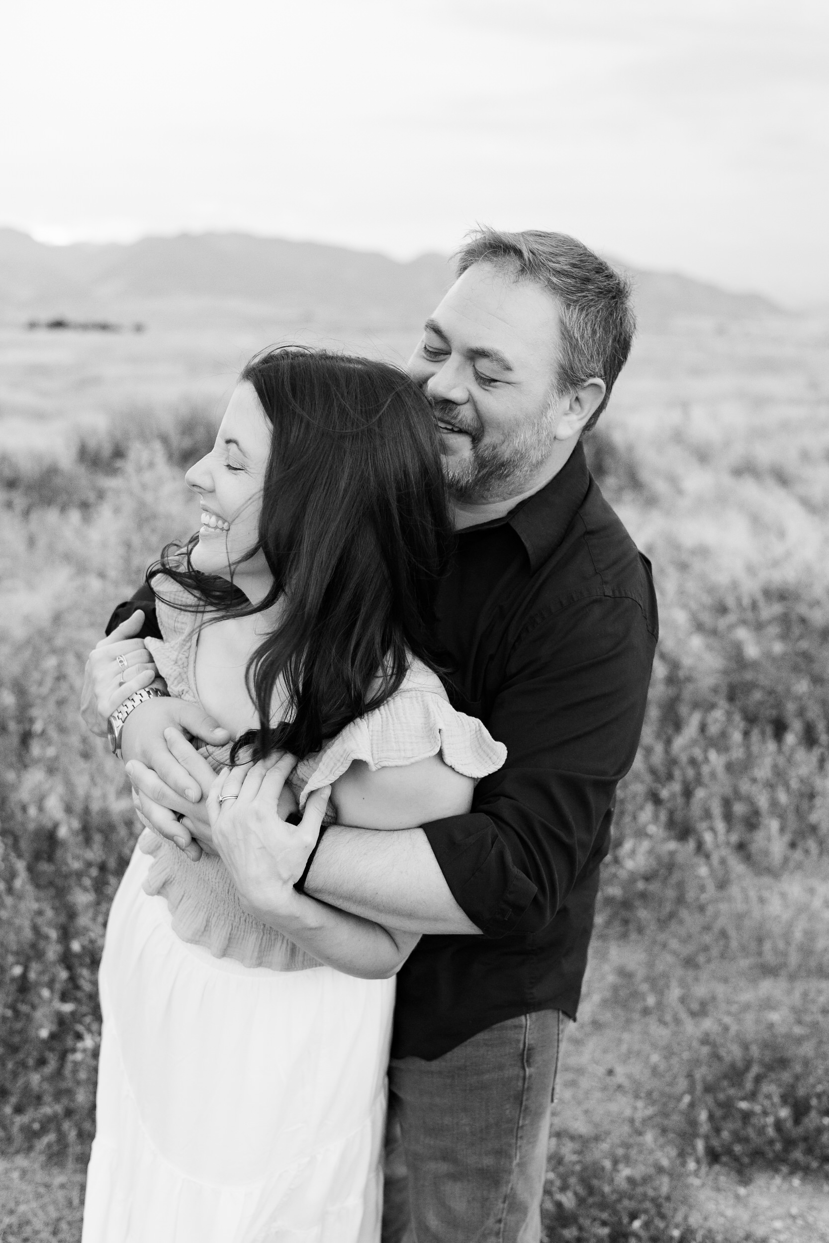 Husband hugs wife around shoulders as she laughs.