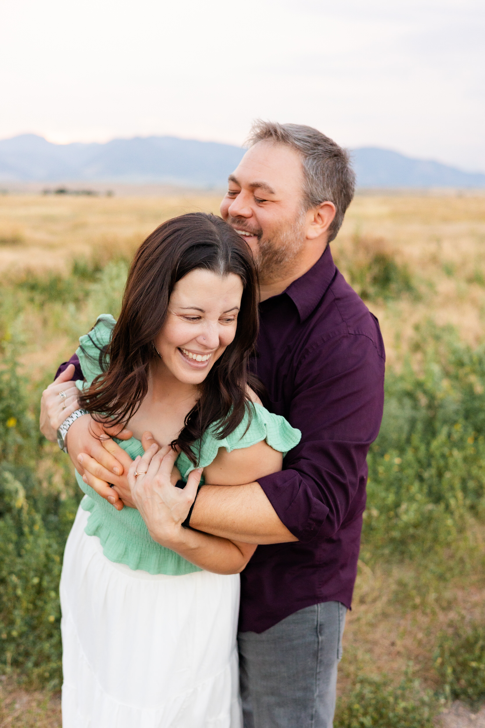 Husband hugs wife around shoulders as she laughs.