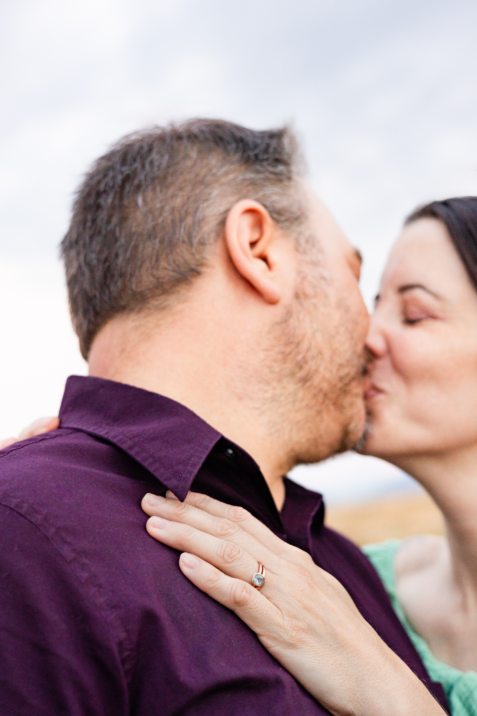 Husband and wife share a kiss with focus on wife's wedding ring