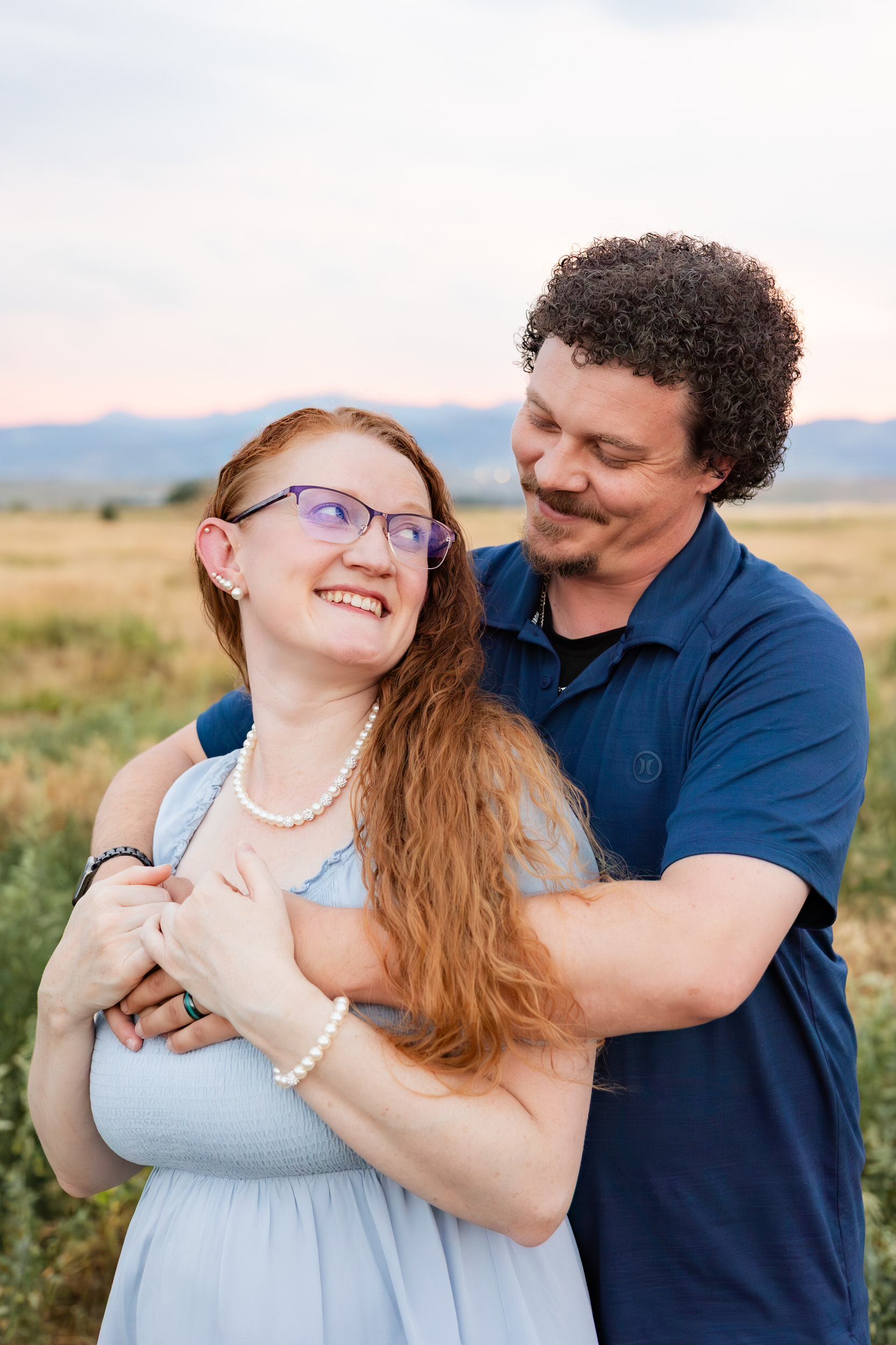 Husband hugs wife around her shoulders and she smiles at him.