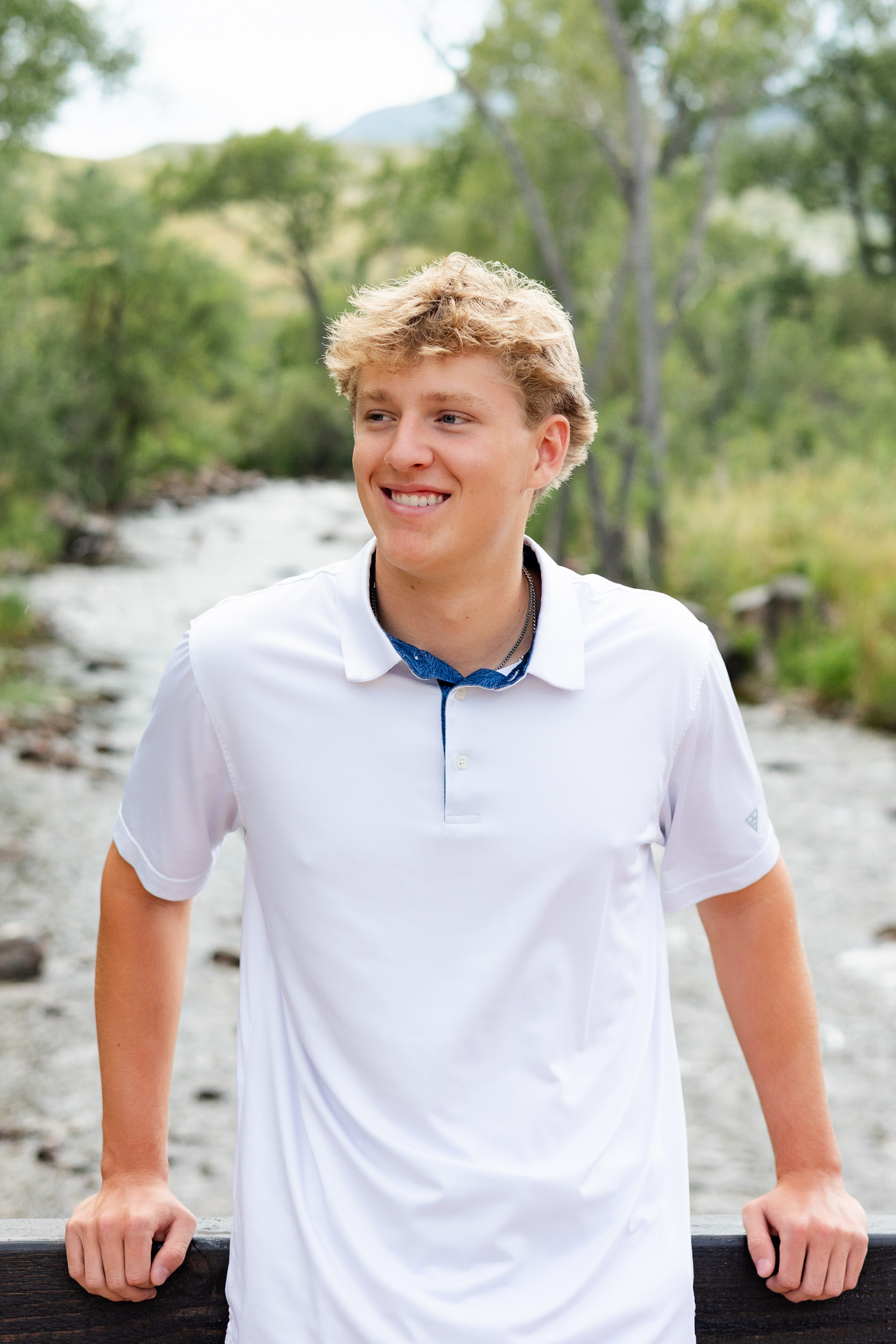 A young man standing on a bridge smiles off camera
